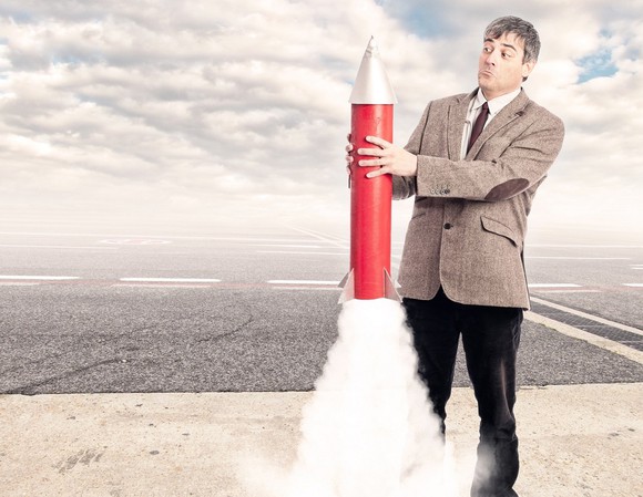 Man with a surprised expression holding a toy rocket that starts to launch.