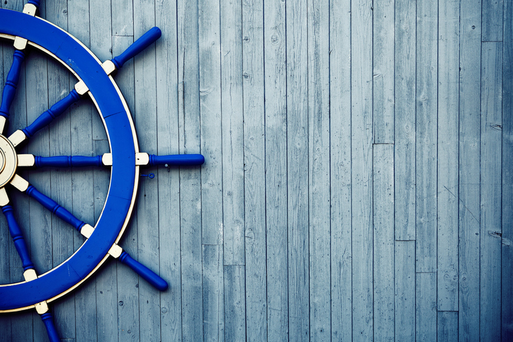 An antique boat helm wheel painted blue rests on a weathered wooden deck.