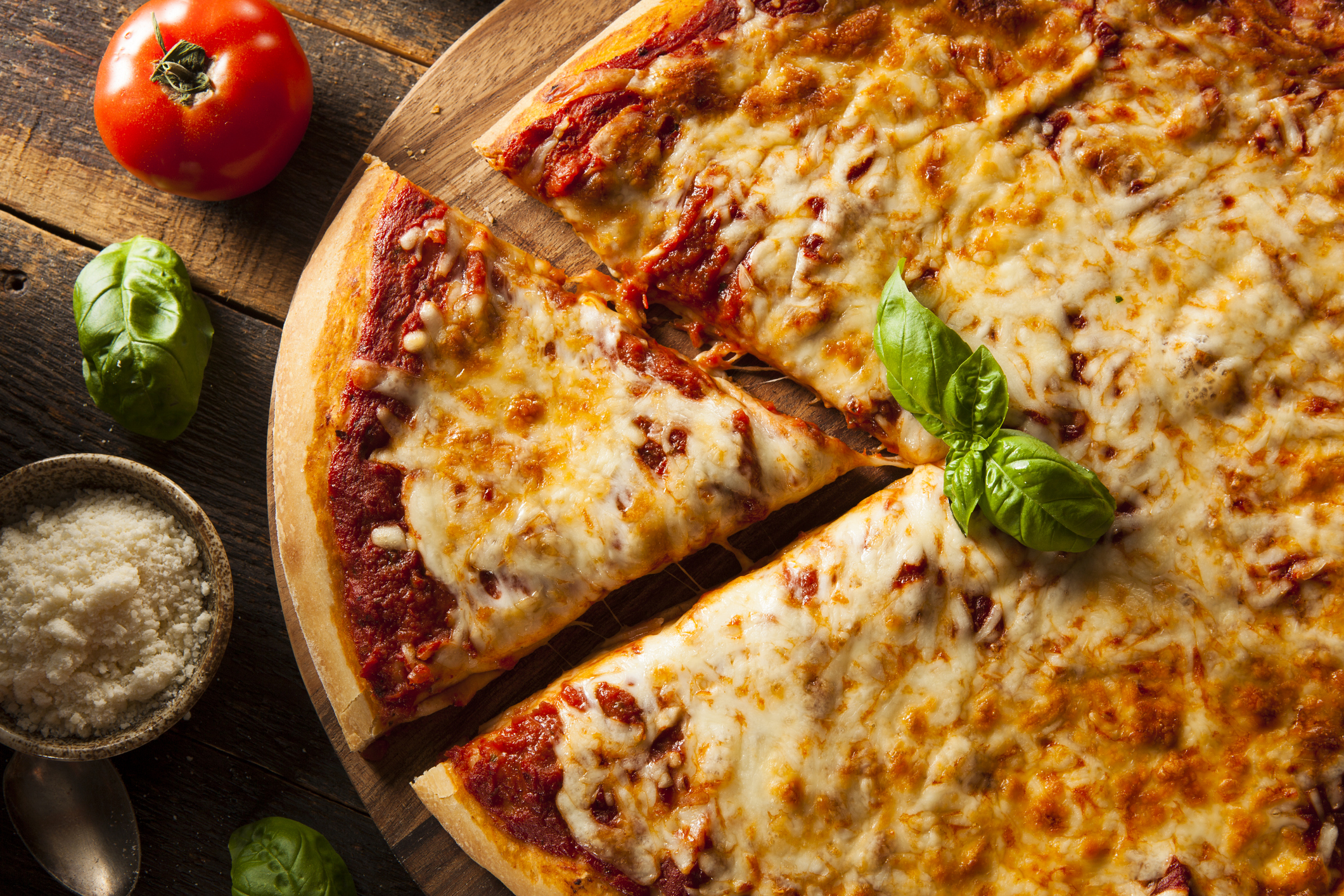 A homemade cheese pizza surrounded by fresh ingredients on a wood table.