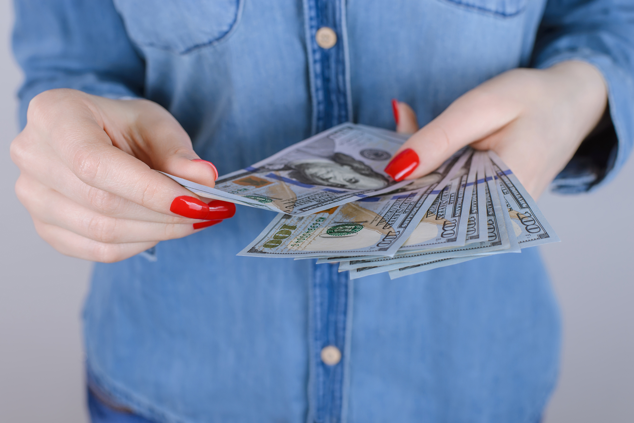 Person with fingernails painted red holding a bunch of hundred-dollar bills.