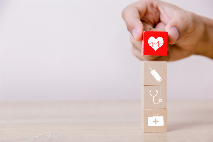 A hand placing a red wooden block with a heart on its face atop several blocks with medical icons on them.