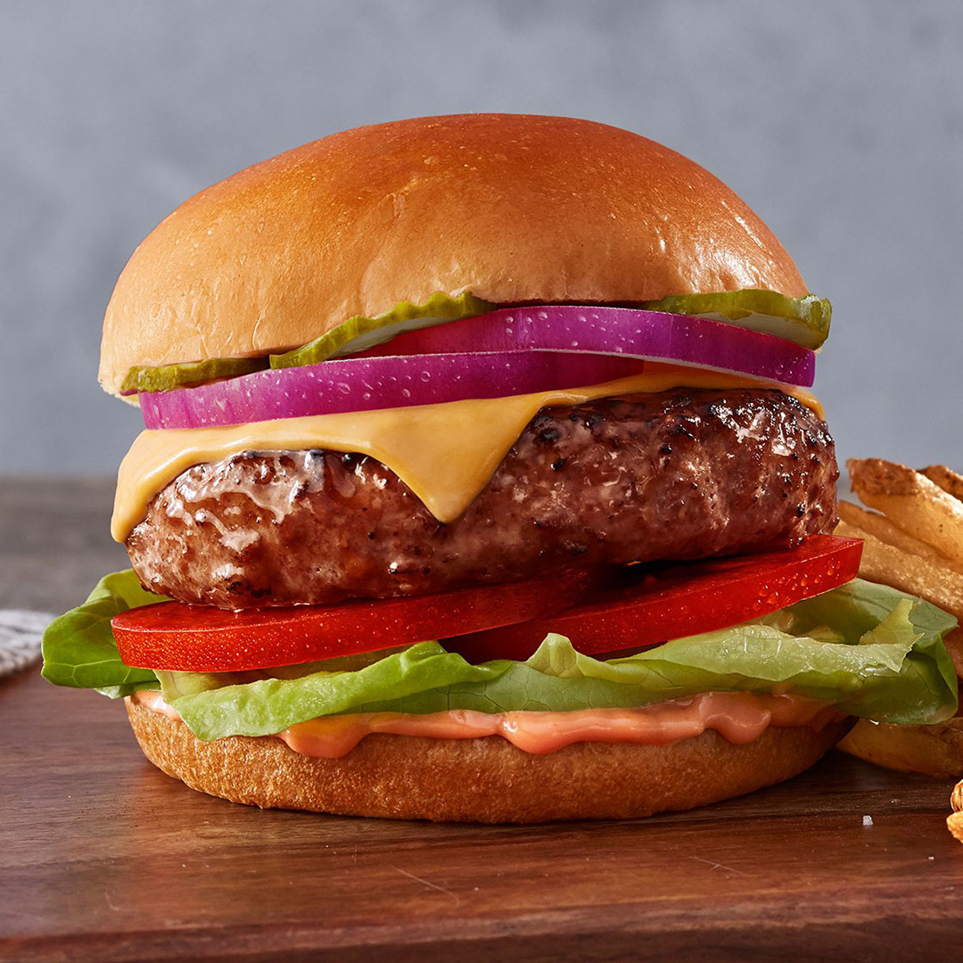 A Beyond Meat burger on a bun with lettuce, tomato, cheese, onions, pickles, and sauce