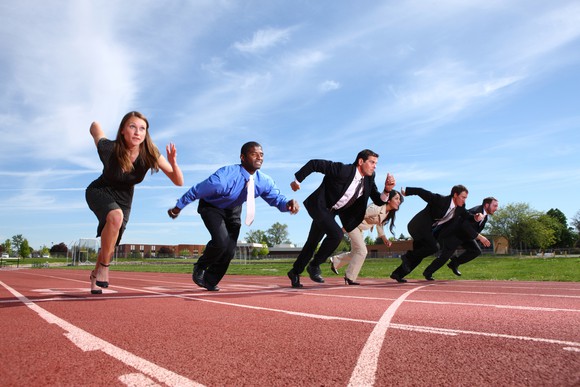 People in business attire taking off running on a track.