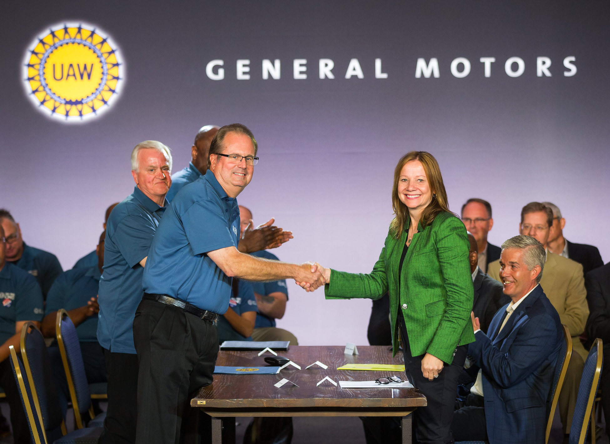 Jones and Barra are shown shaking hands across a conference table.