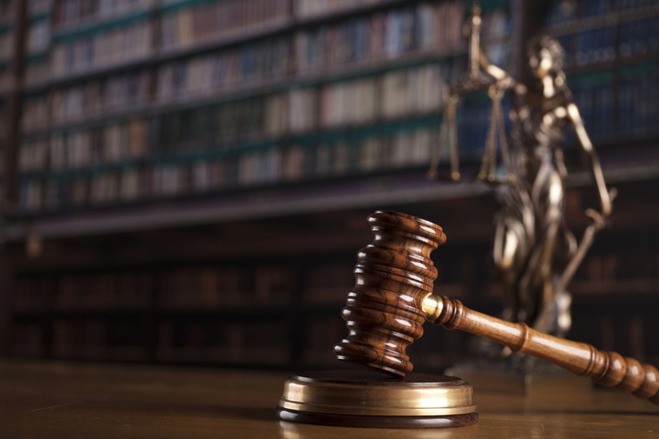 A gavel and a Lady Justice statue on a table with bookcases in the background..