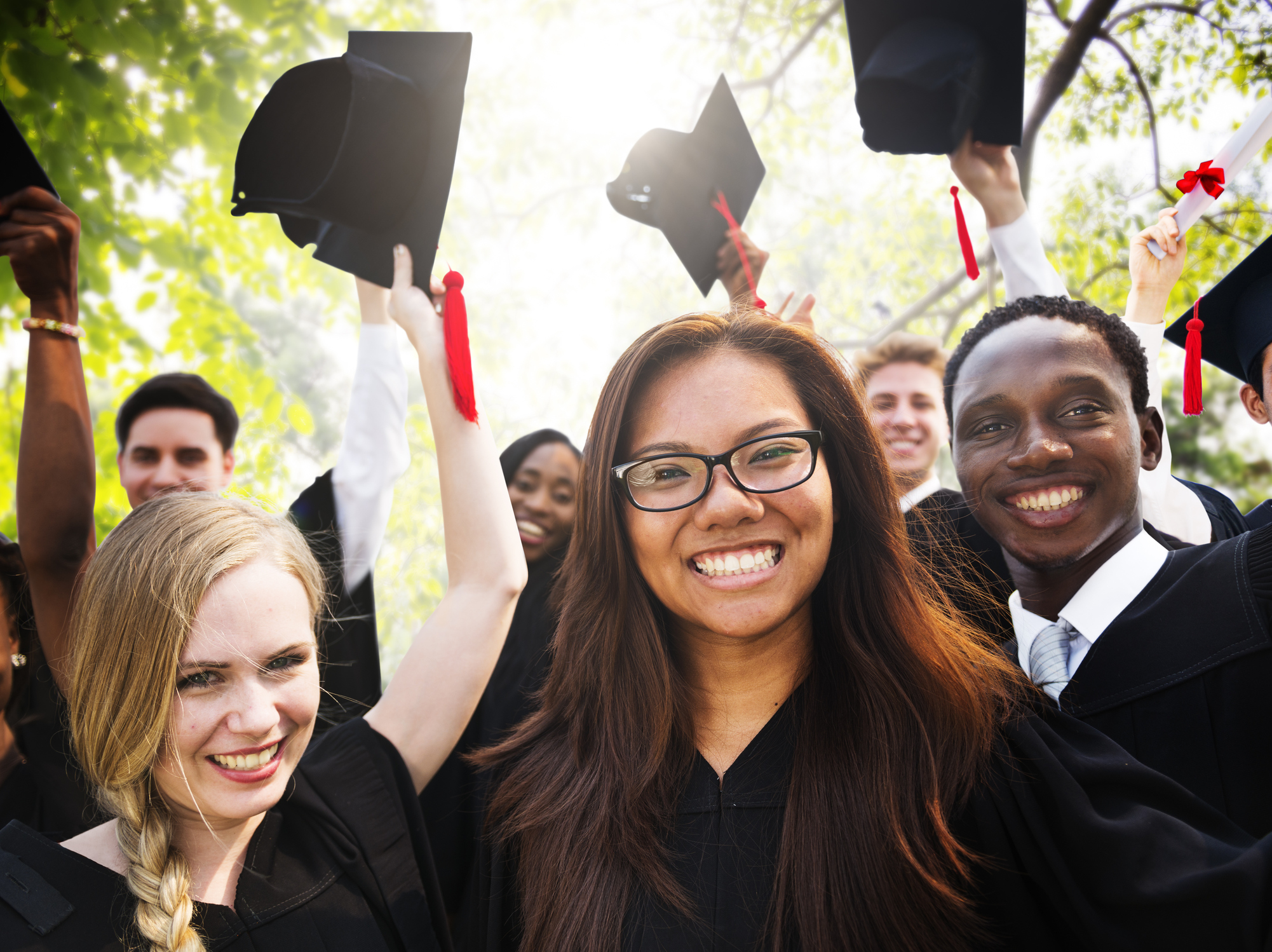 Smiling young adults in graduation gowns waving caps in the air