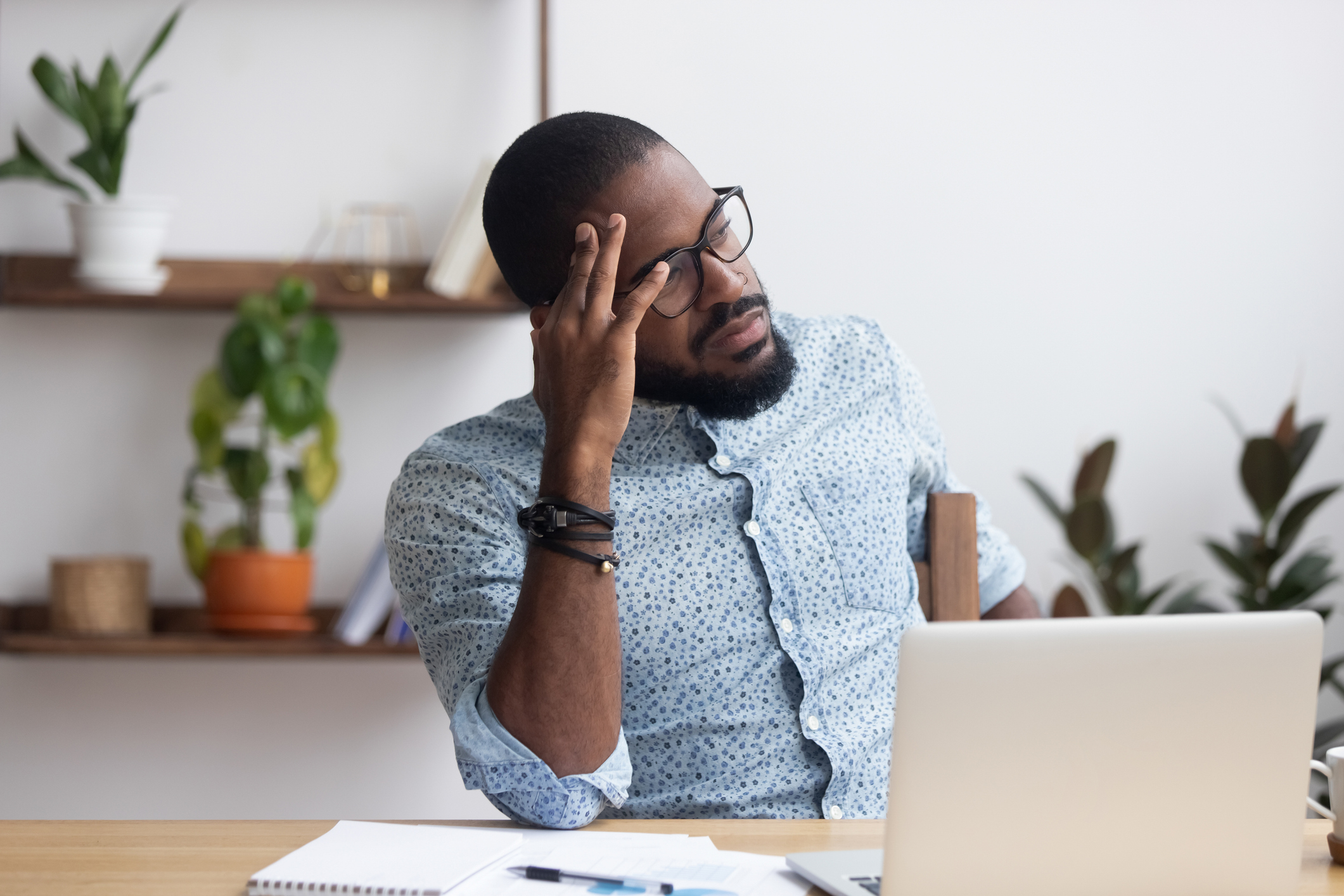 Man sitting at laptop holding his head with annoyed expression.