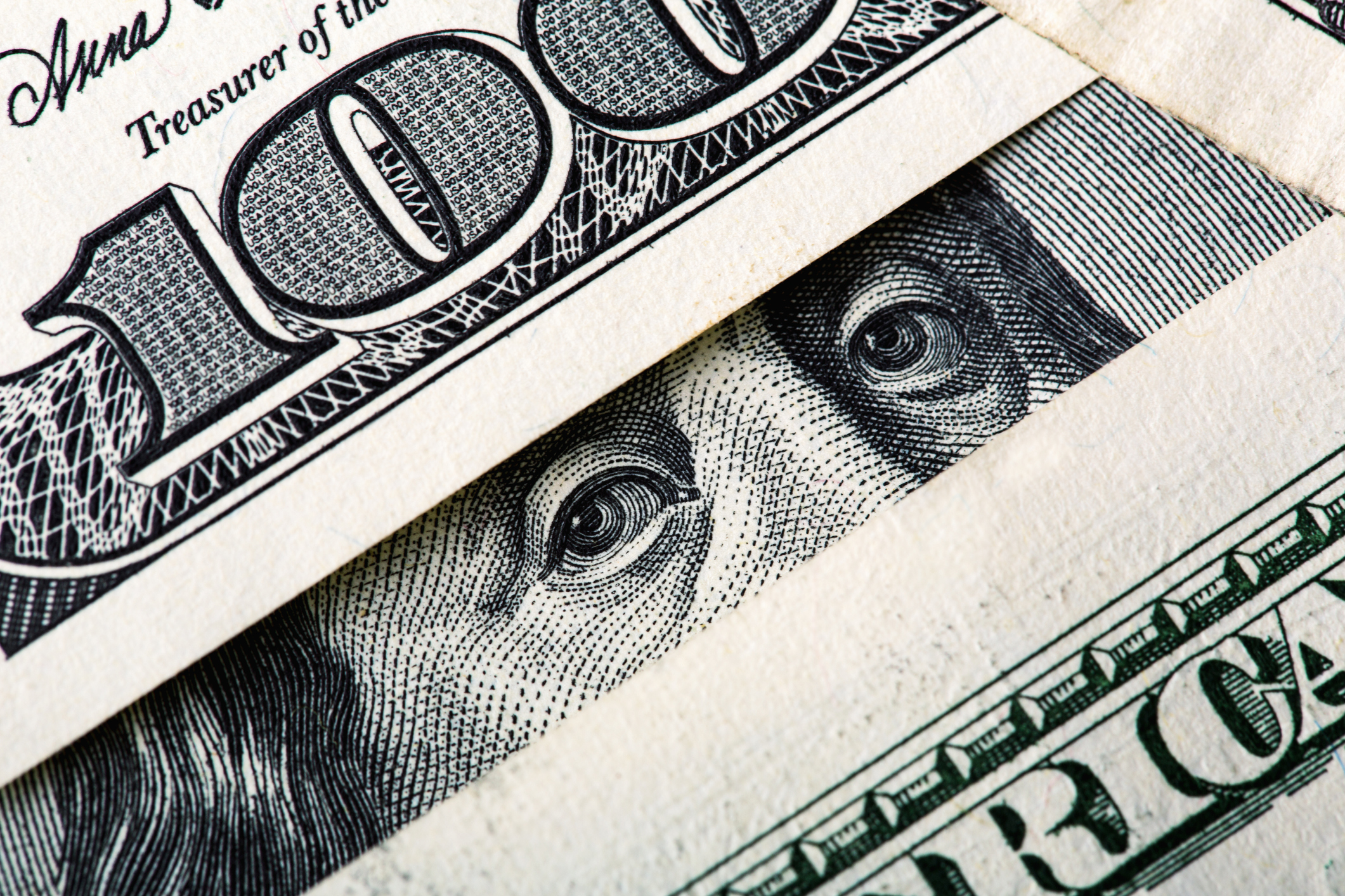 Ben Franklin's eyes peering through a number of one hundred dollar bills.