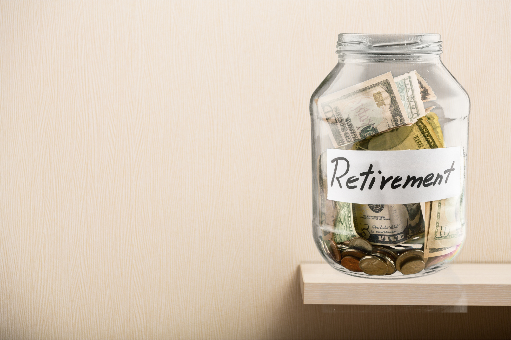 Glass jar with bills and coins in it labeled retirement