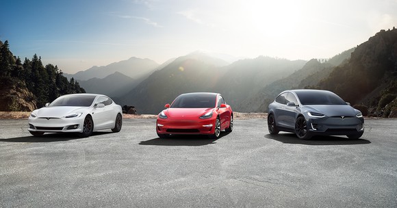 Tesla Model S, Model 3, and Model X lined up with mountains in the background.