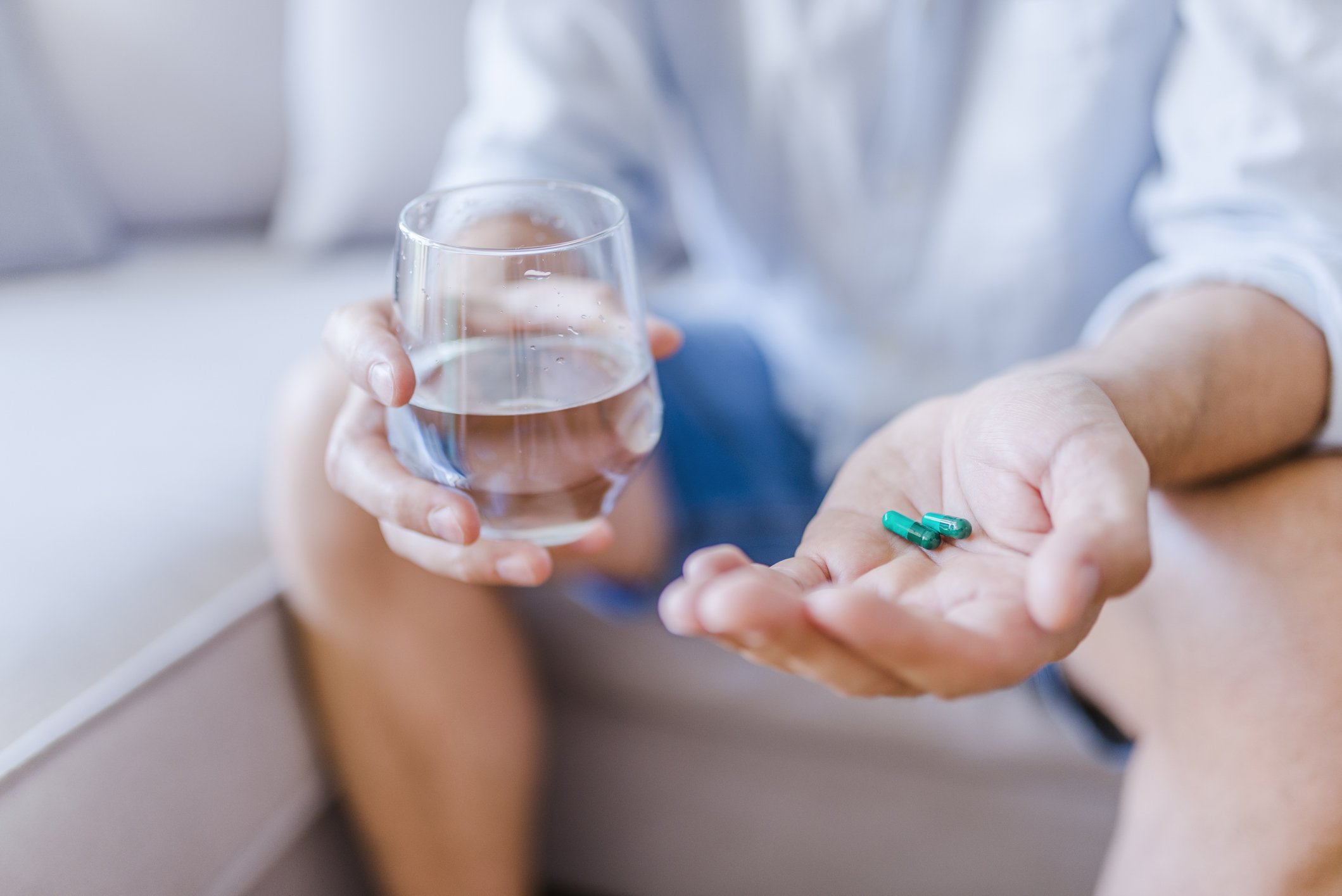 Man holding water glass in one hand and blue pills in the other hand
