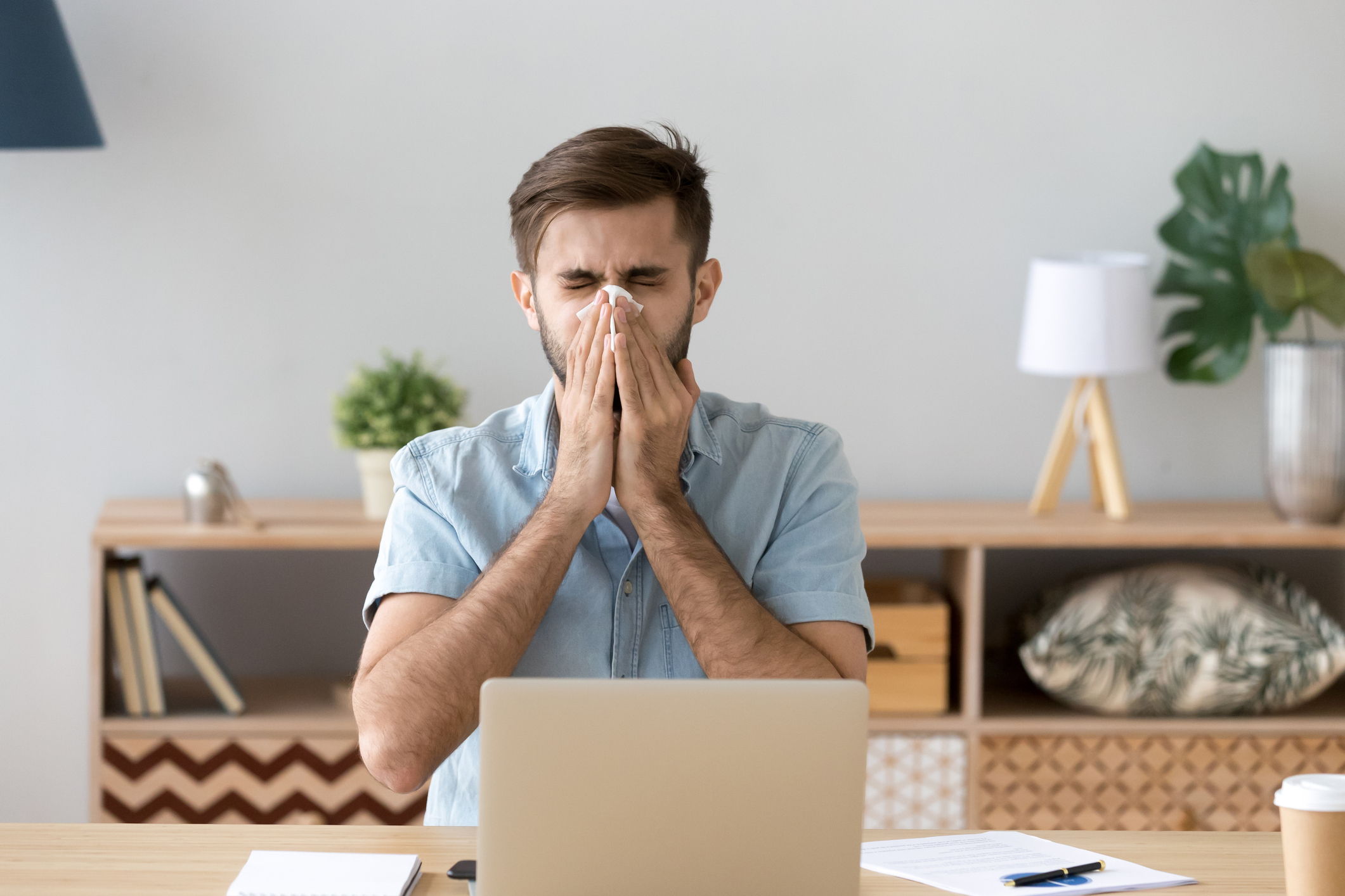 Man sitting at laptop, blowing his nose