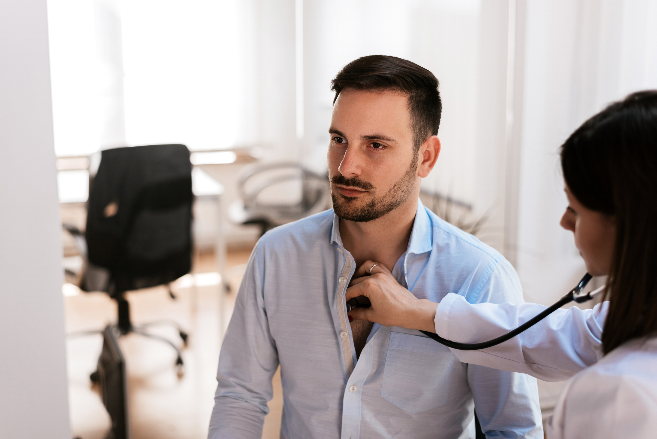 Woman in white coat placing stethoscope on man's chest