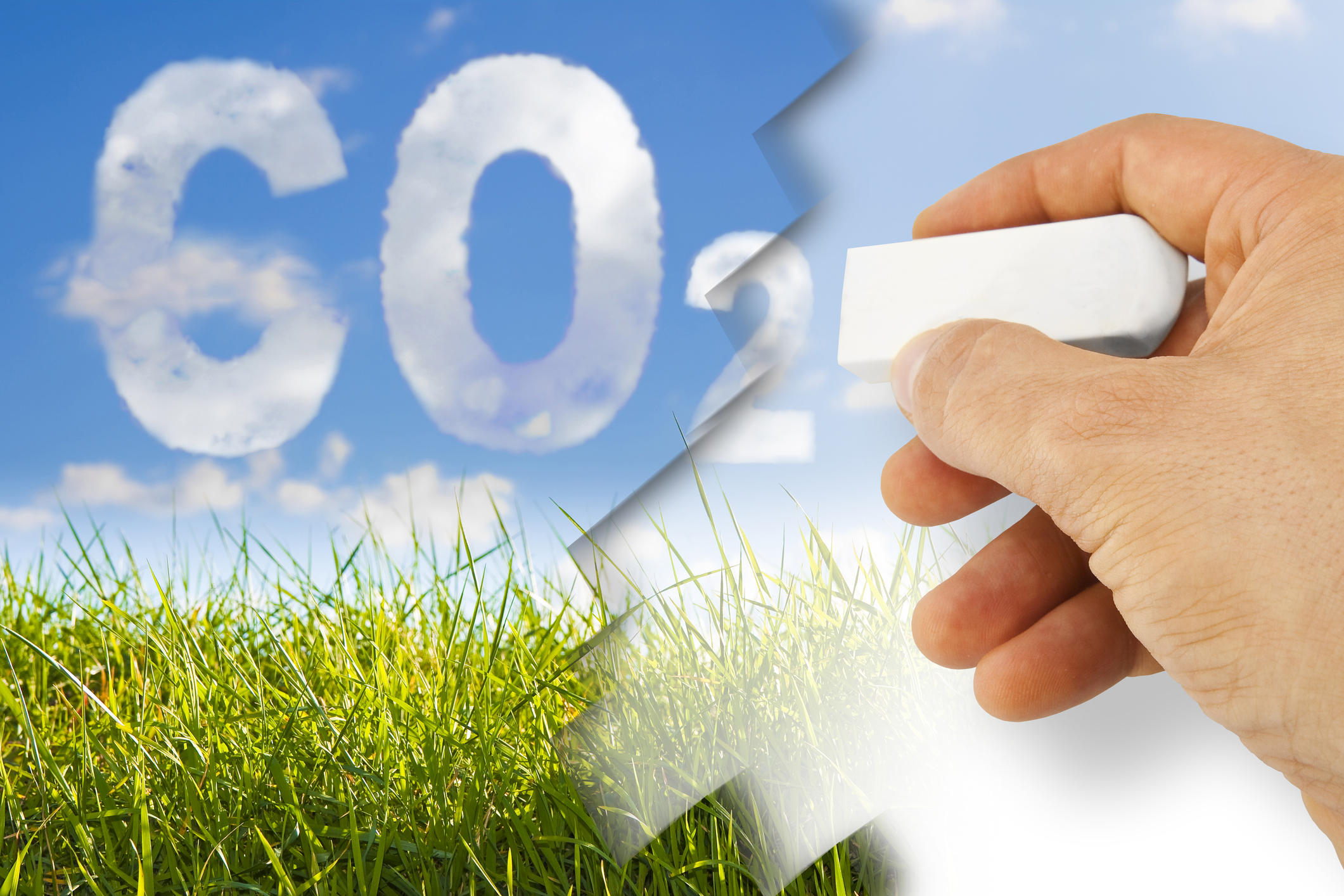 A hand with an eraser removing carbon dioxide, with green grass and a blue sky in the background.