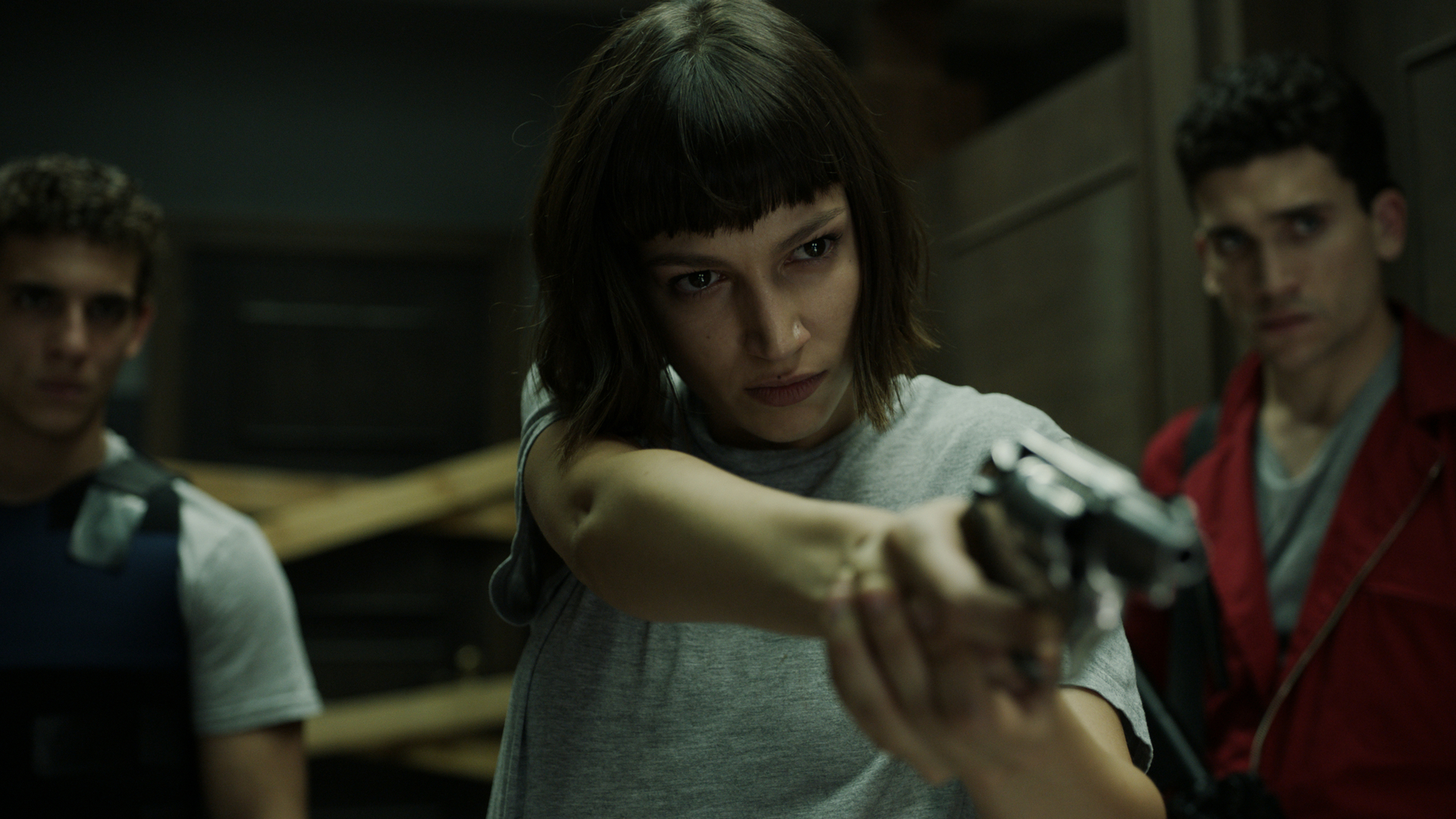 A woman points a gun at an unseen foe as two men look on.