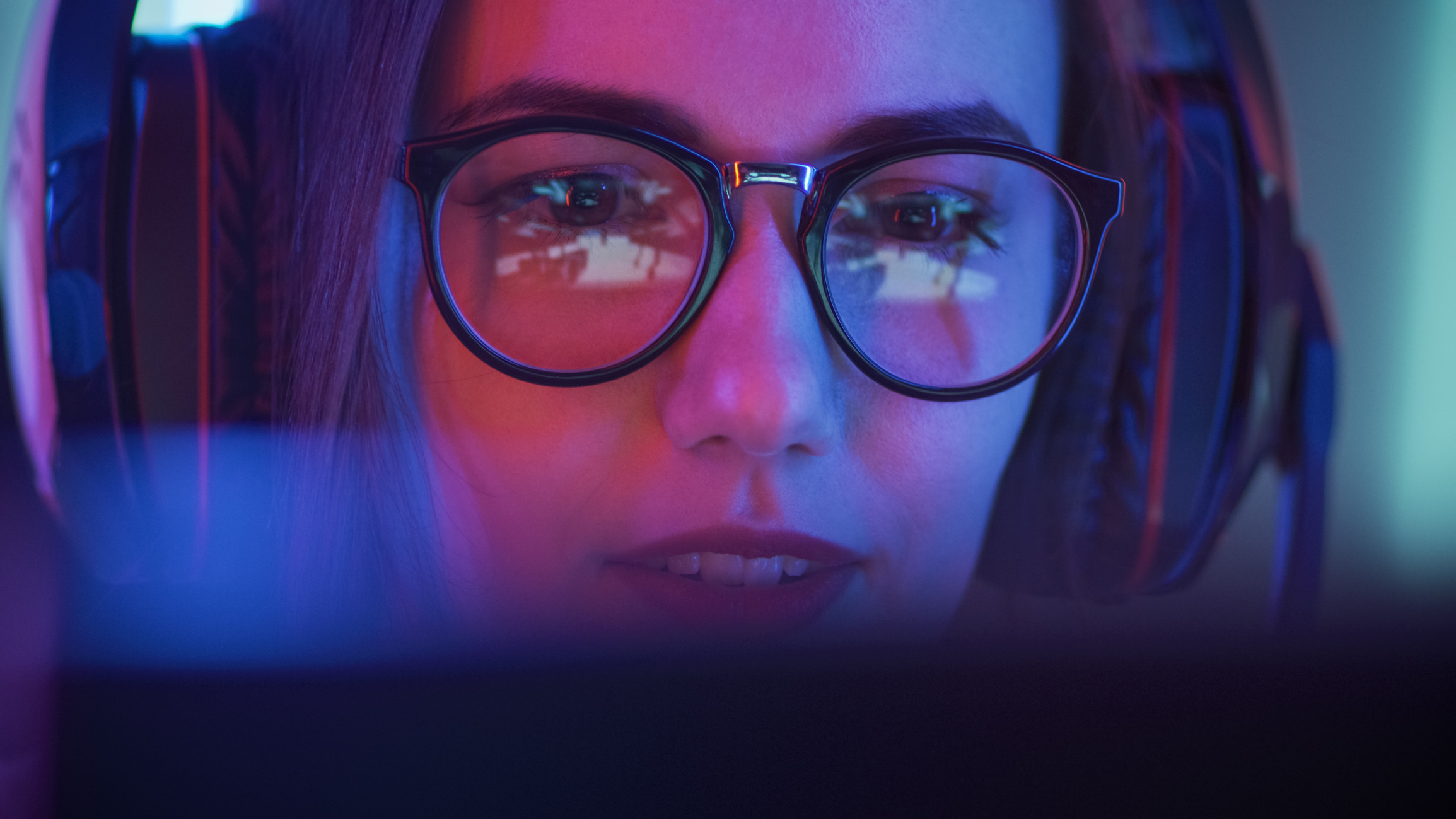 A woman in glasses plays a game on a PC.