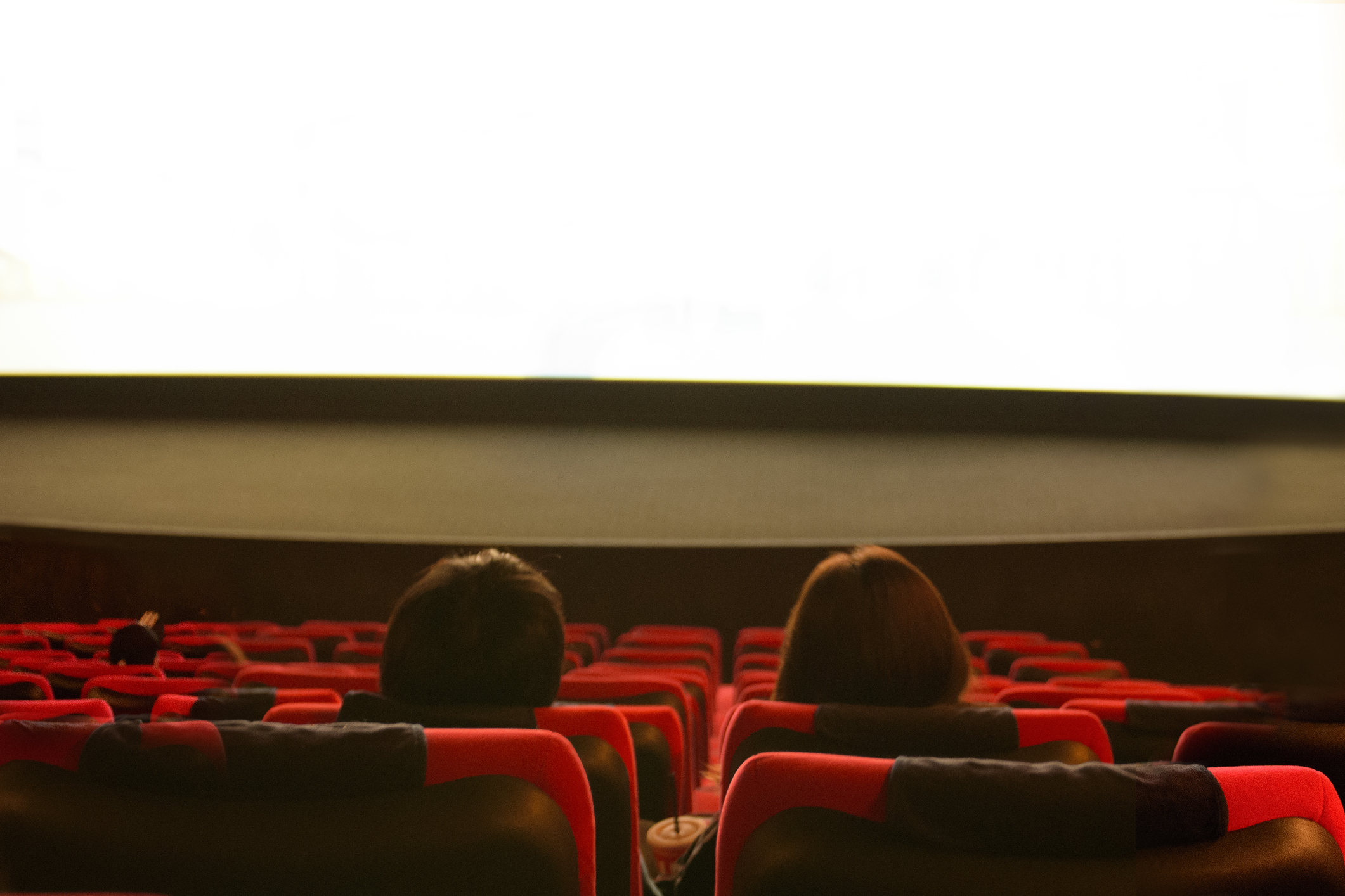 Two people sitting in a movie theater looking at the screen.