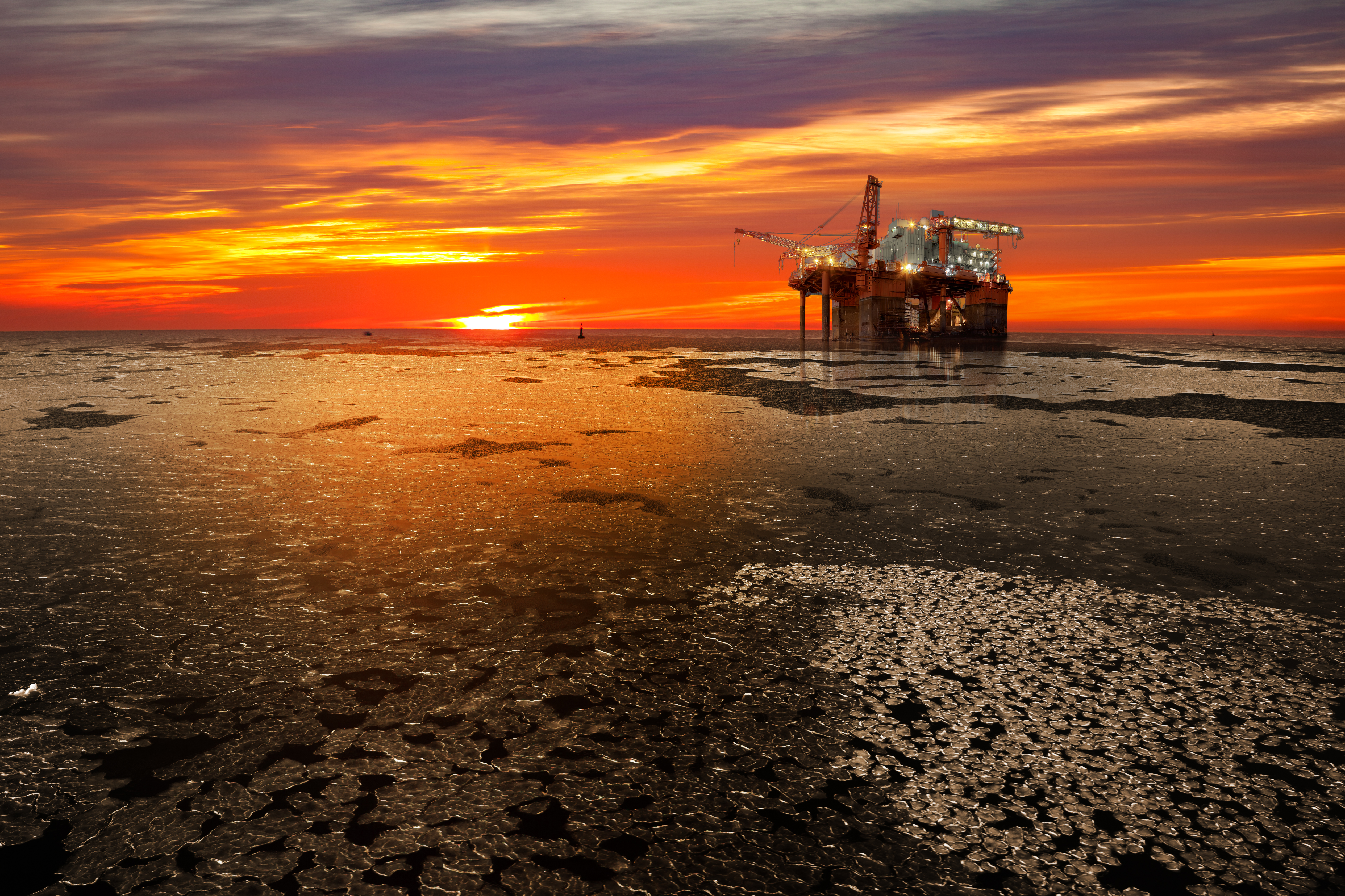 An offshore drilling rig with a bright sunset in the background.
