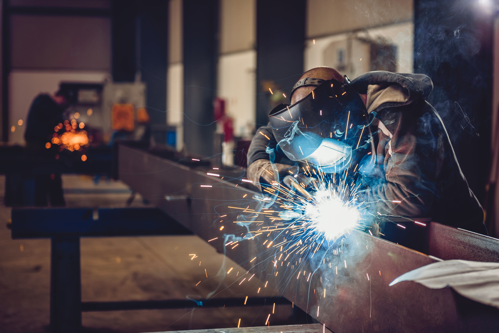 A worker in a protective suit solders a large steel beam.