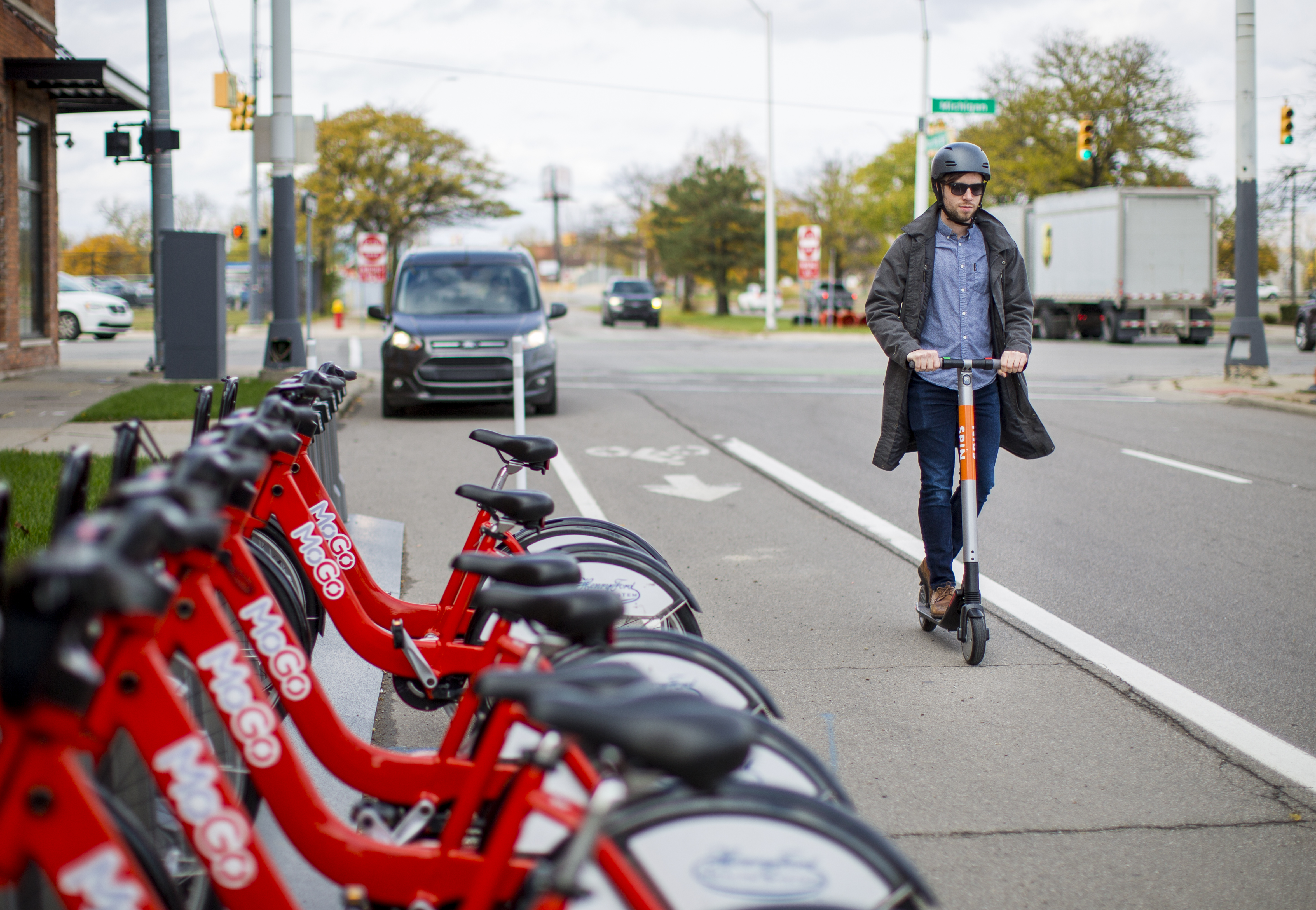 Man riding a scooter in front of a row of parked bikes.