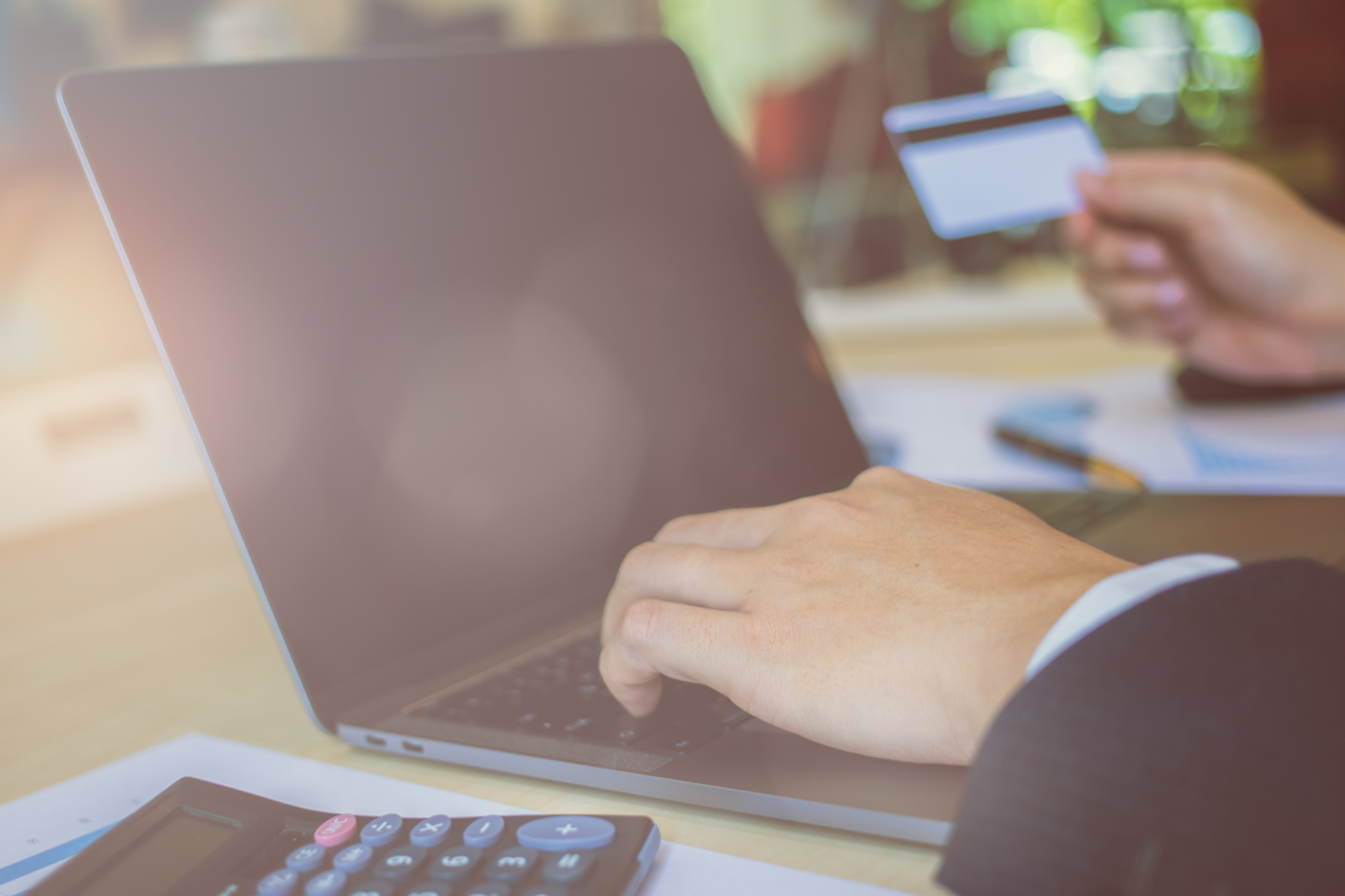 One hand touching a computer and making a payment, while the other hand holds a credit card.