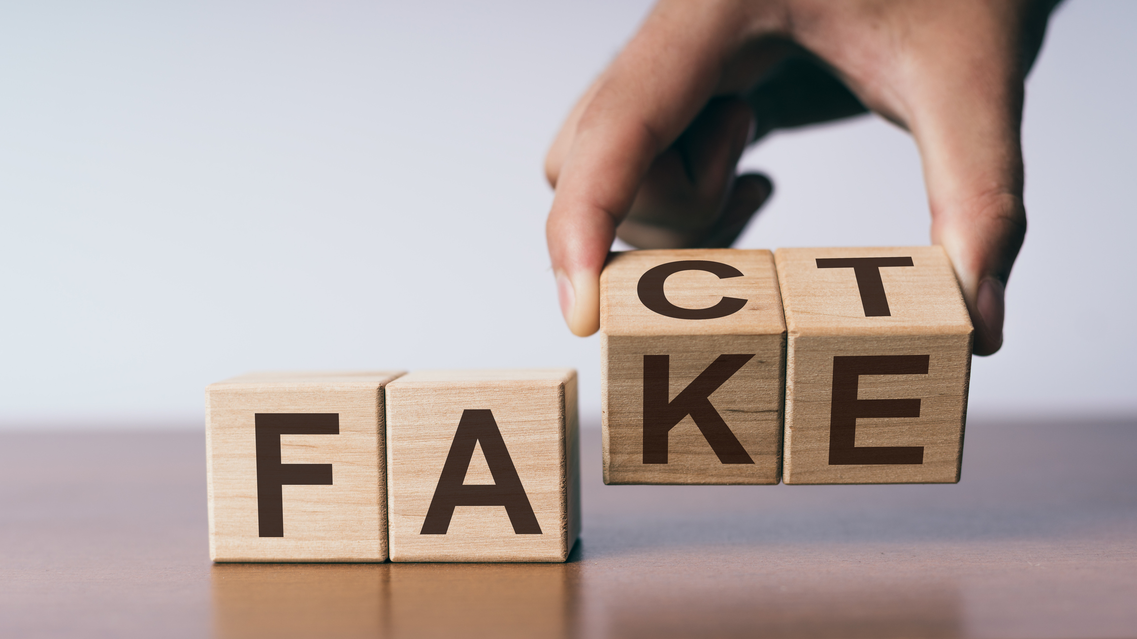 A person holding four wooden blocks that spell fake or fact.