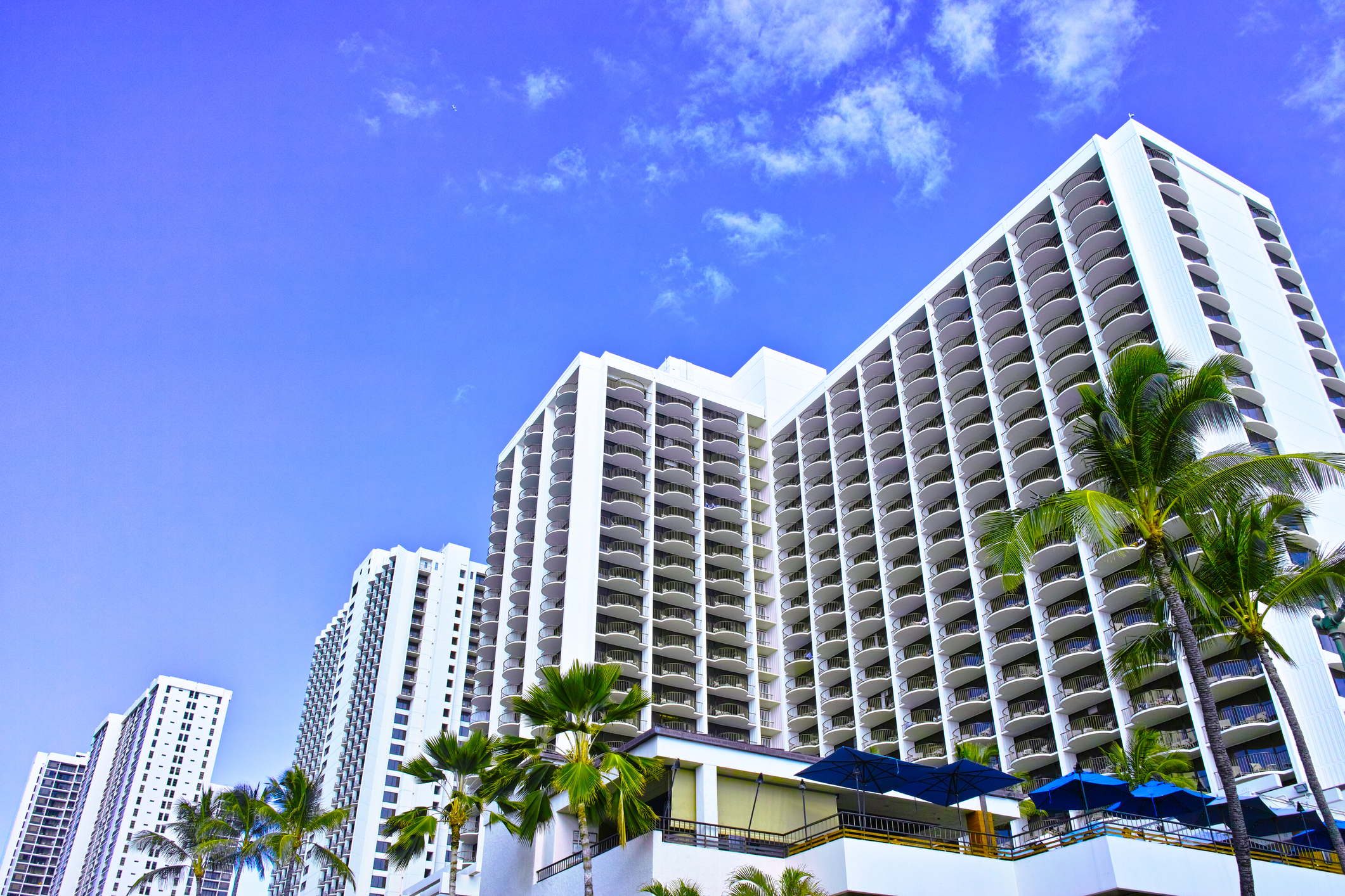 A multi-story hotel complex with white facade, flanked by palm trees.