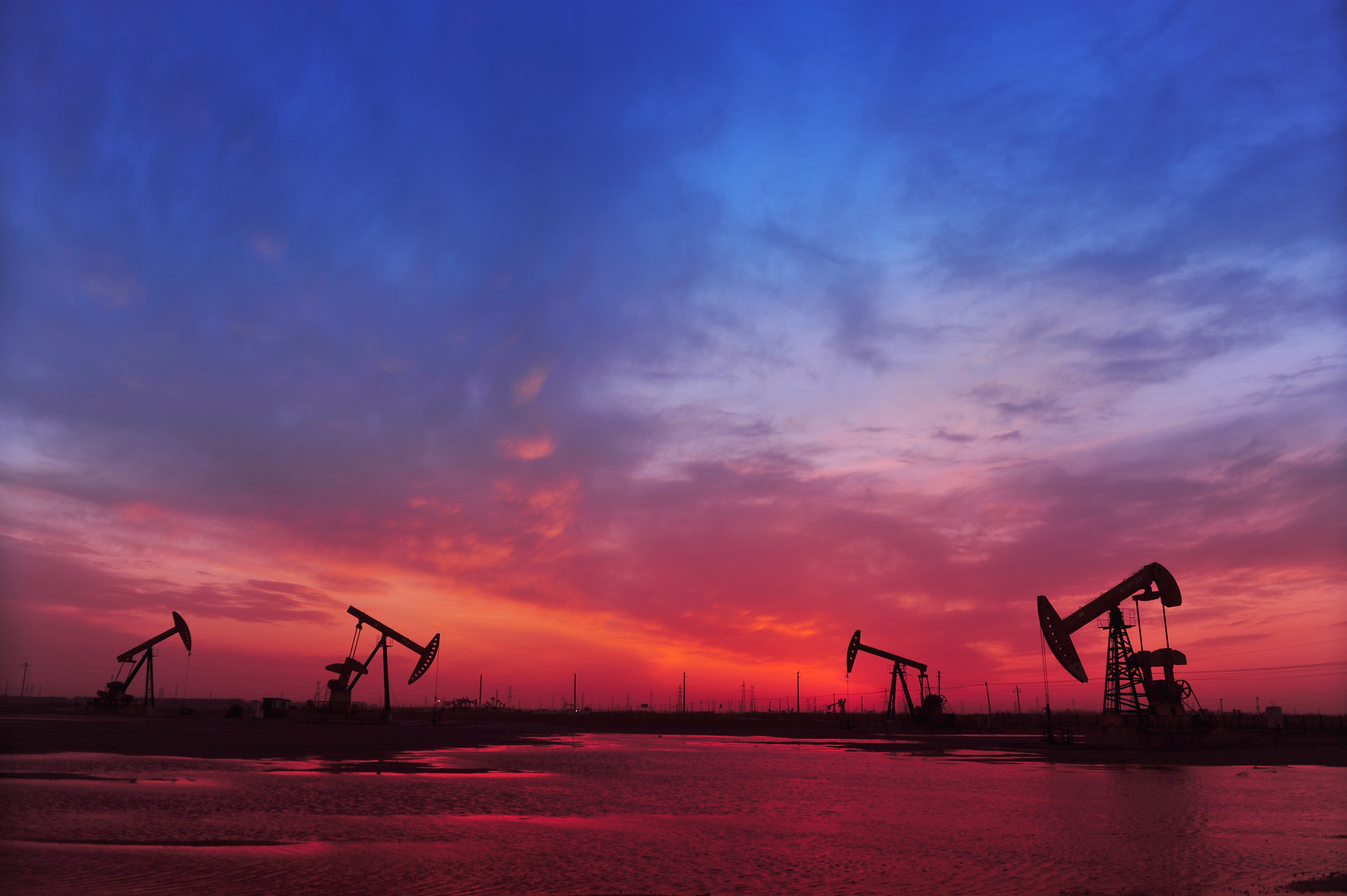 Several oil pumps in front of a red and blue sky.