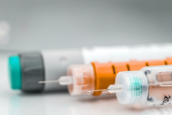 Two insulin injection needles and one insulin pen lined up on a table.