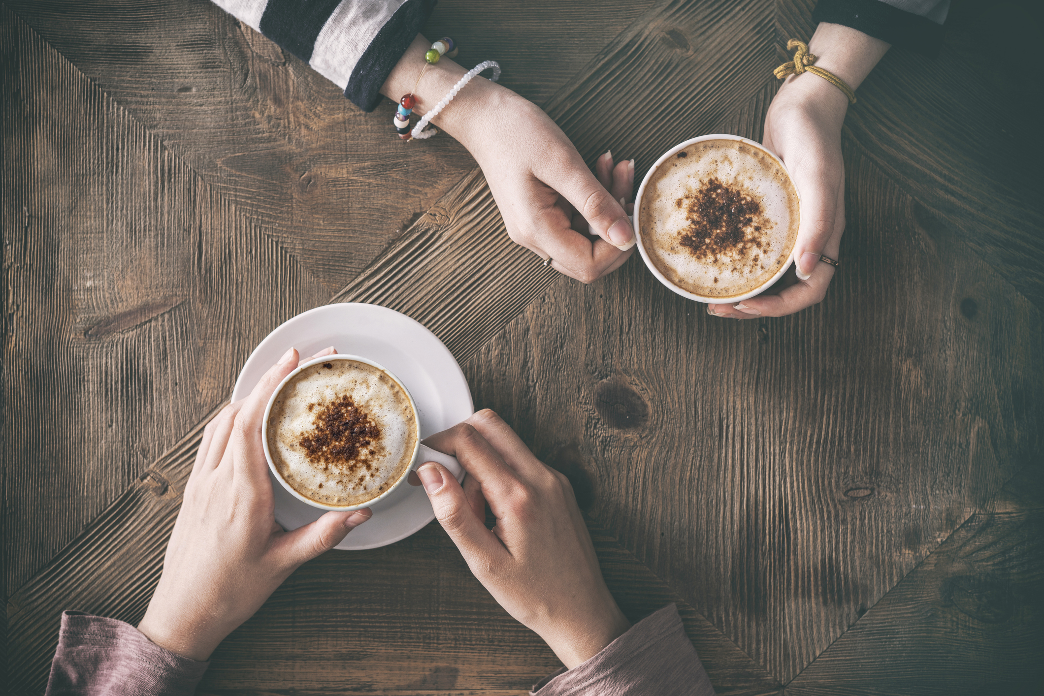 A bird's eye view of two people holding cups of coffee on a table