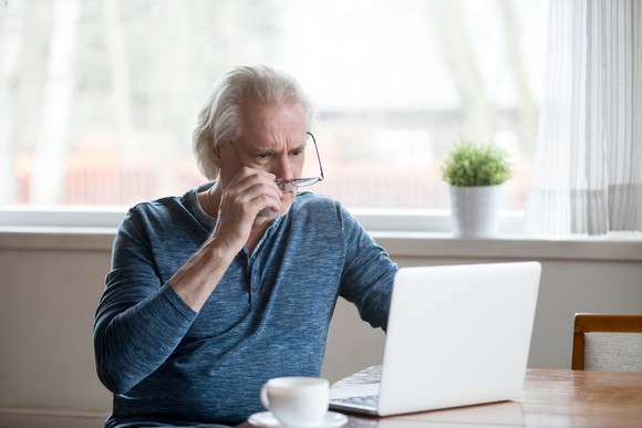 Shocked senior man removes glasses to look at laptop
