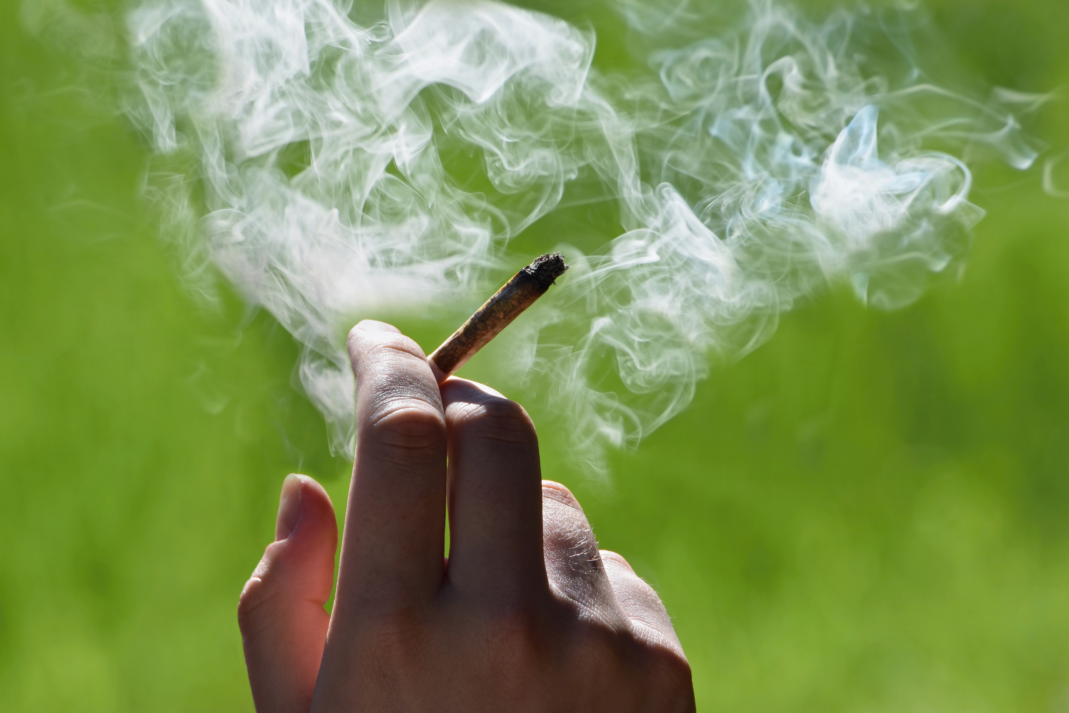 Hand holding cigarette with smoke wafting from the cigarette