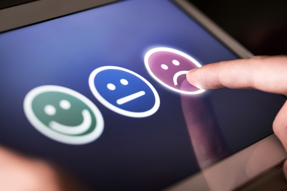 Finger pointing to a frowning face icon on a touchscreen pad next to a straight-face icon and a smiling face icon