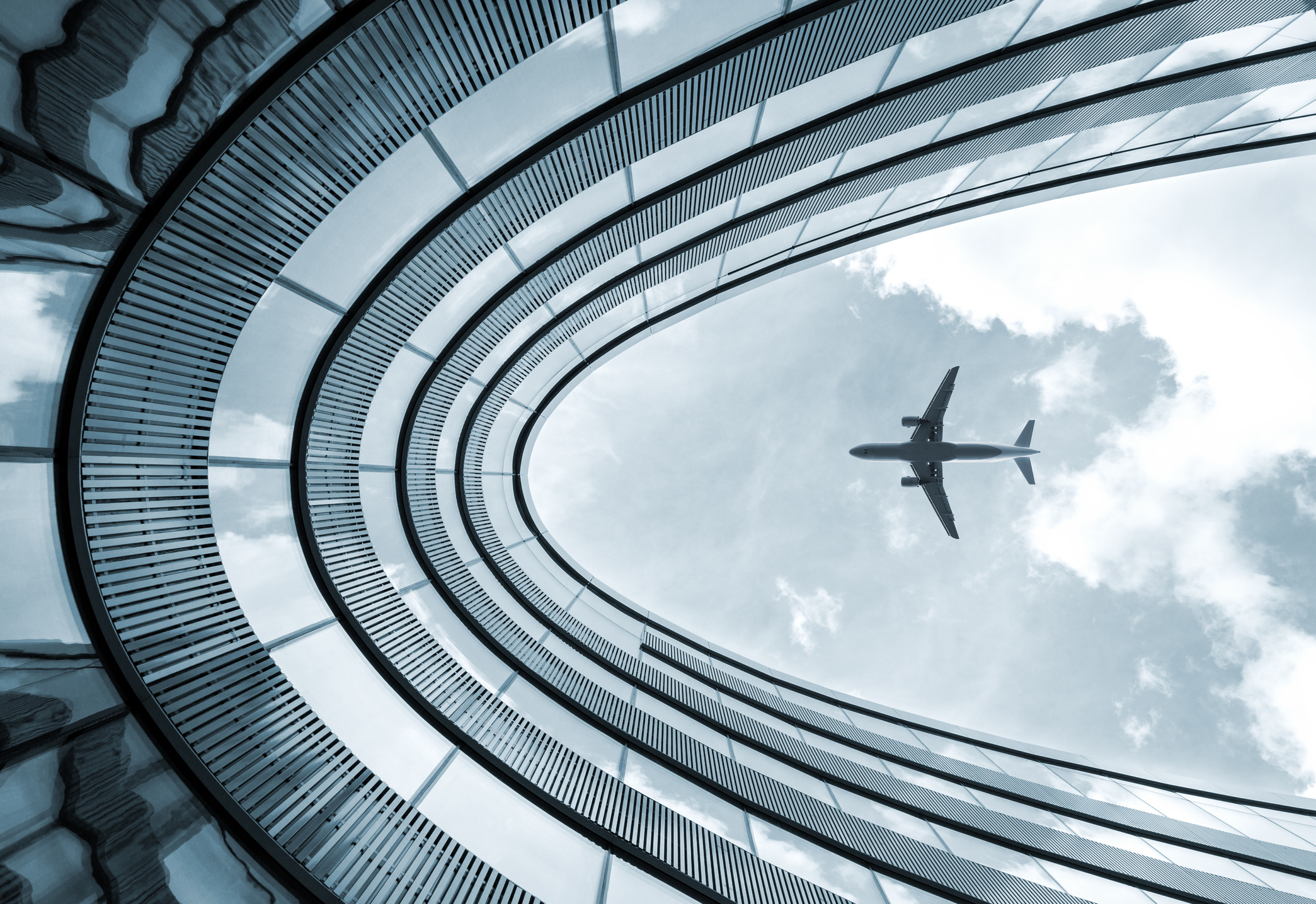 An aircraft flies over a modern office building on approach for landing.