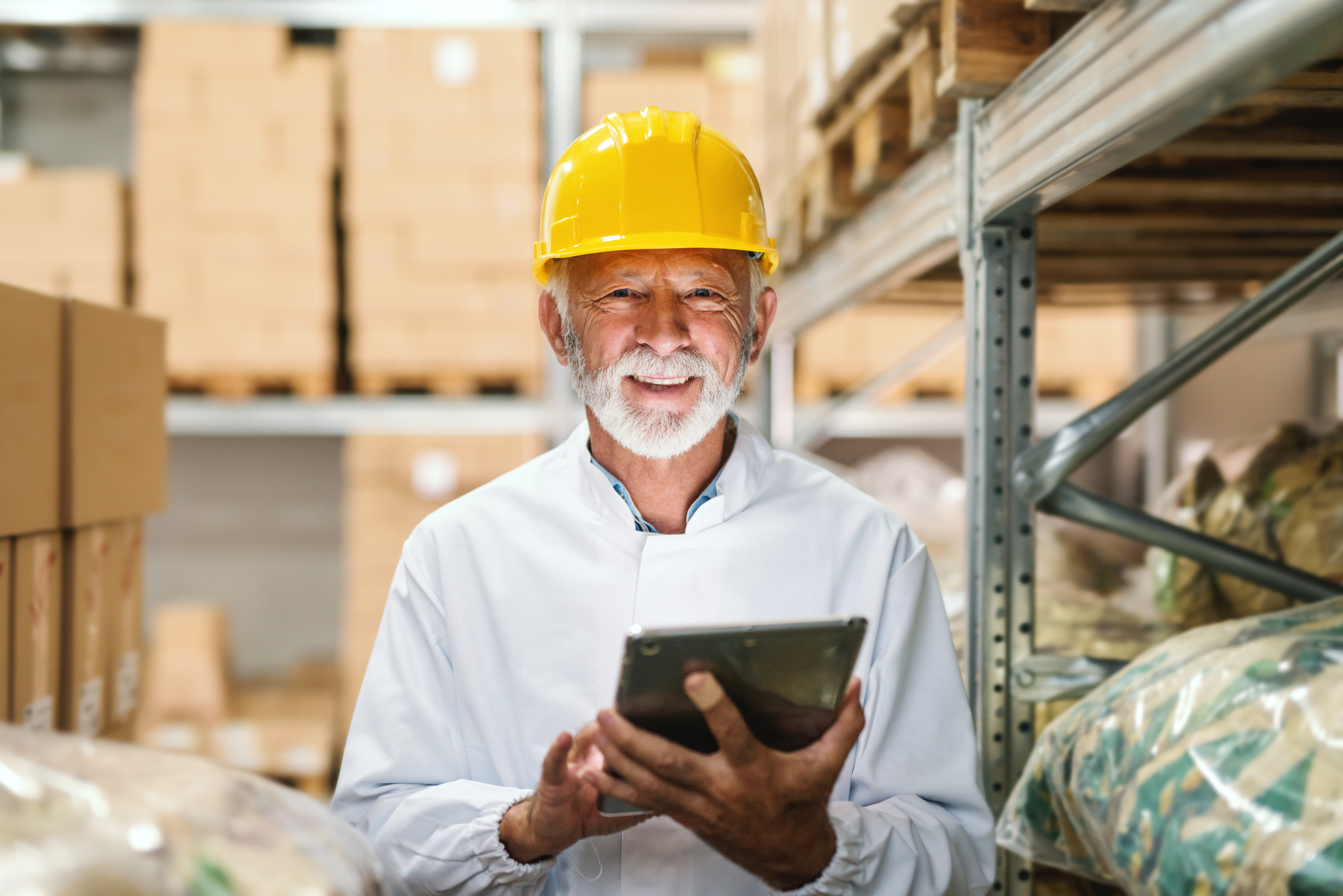 Smiling older man wearing yellow hard hat in warehouse