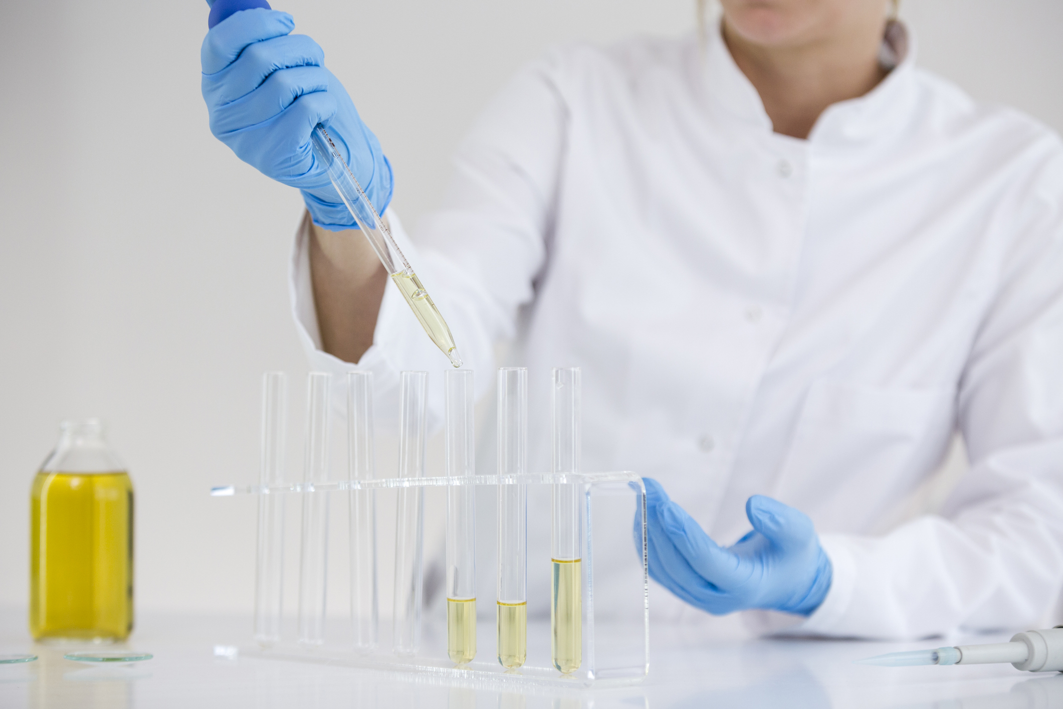 Scientist in a lab coat putting oil in test tubes.