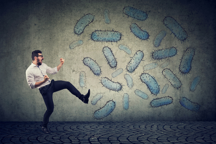 A man in a defensive pose standing next to bacteria painted on a wall.
