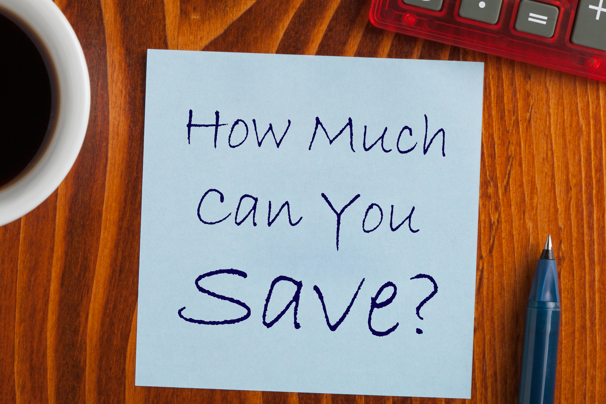 "How much can you save?" written on a square of paper on a table near a coffee cup and a pen