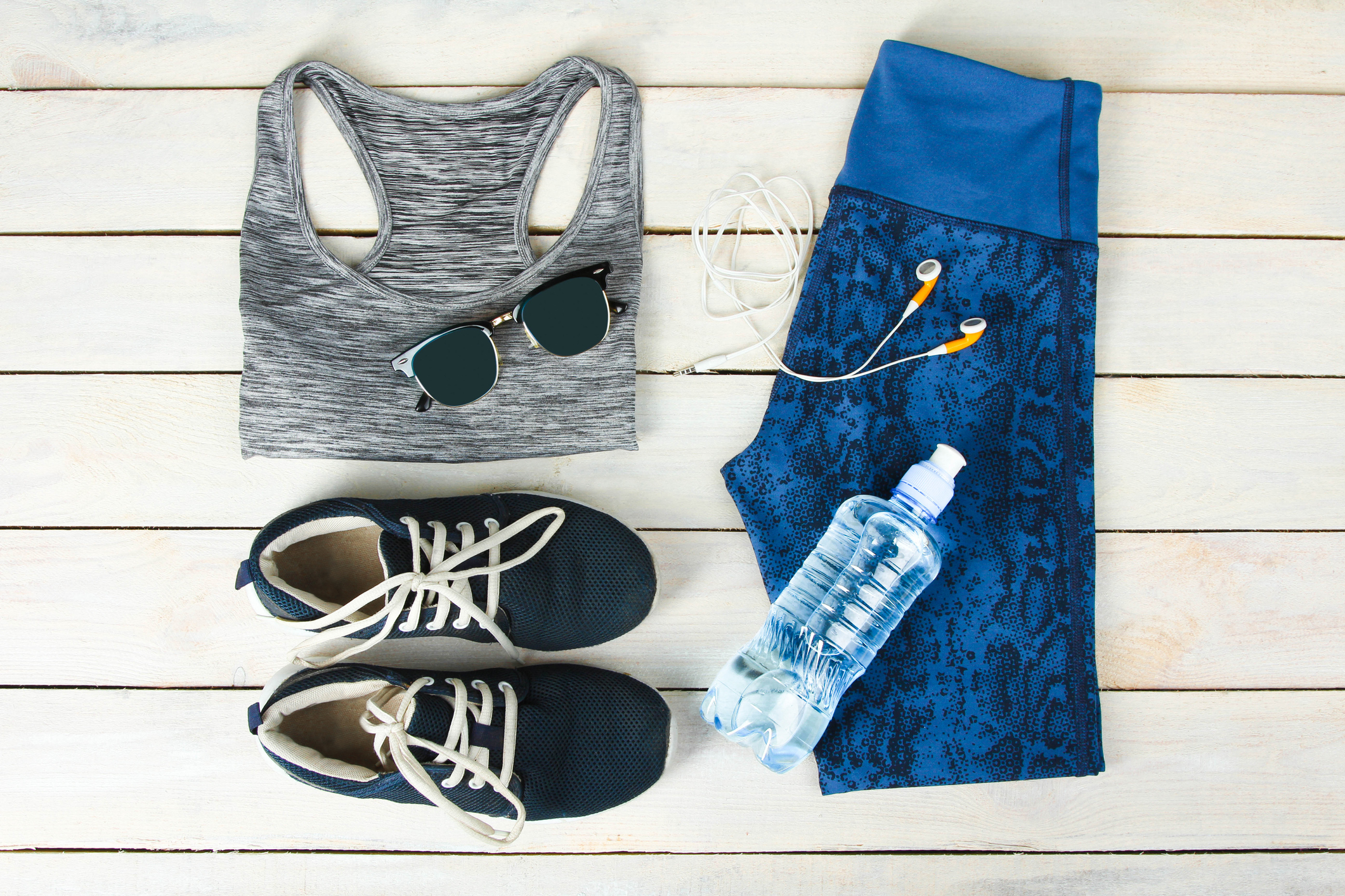 A sports bra, sunglasses, sneakers, water bottle, earphones, and capris pants laid out on a table.