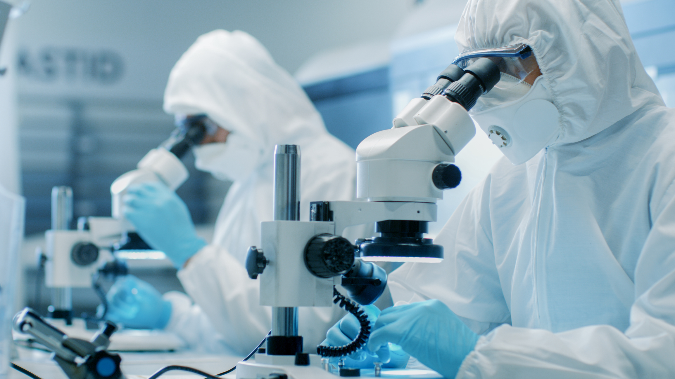 Lab employees with hazard gear and microscopes.