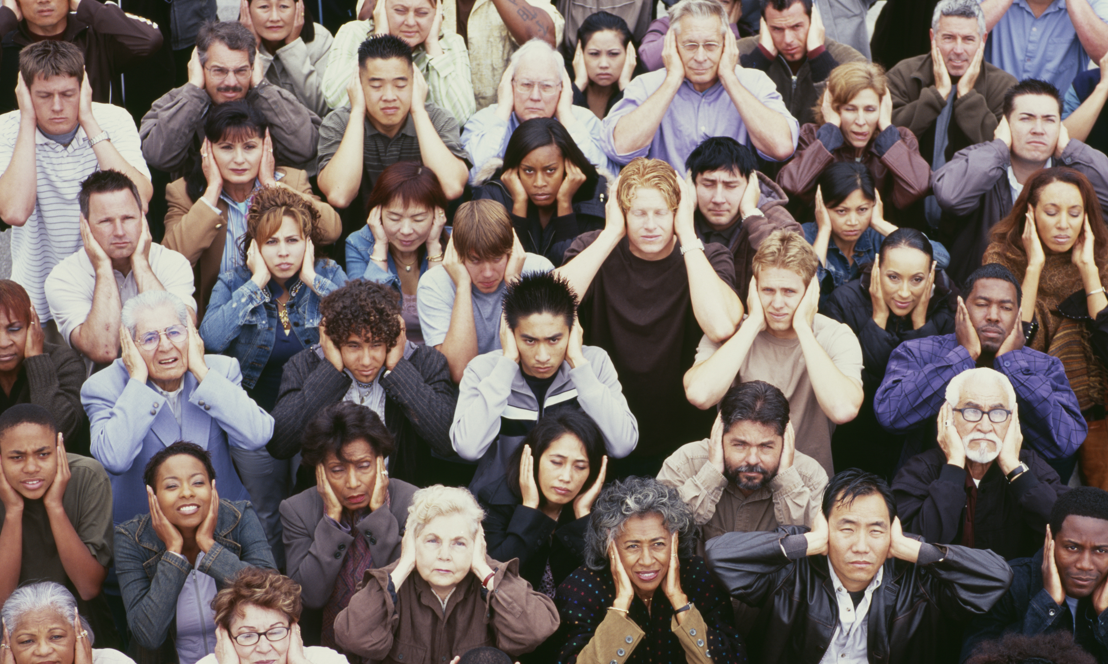 Crowd of people holding their hands over their ears.