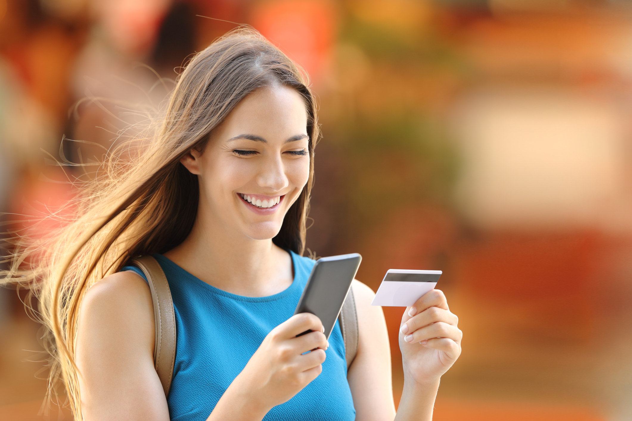Woman looking at her smartphone and credit card while smiling
