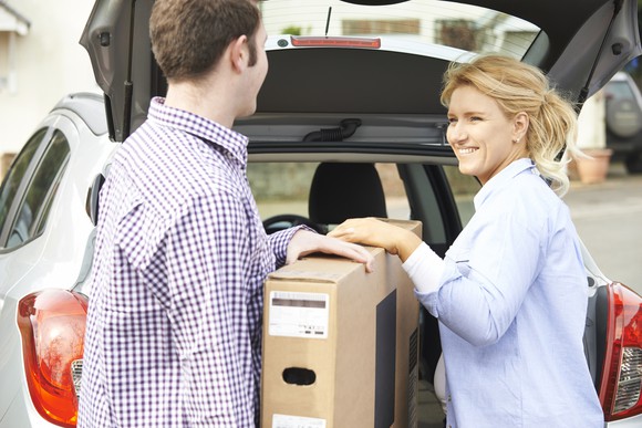 A man and woman loading a package into a car.