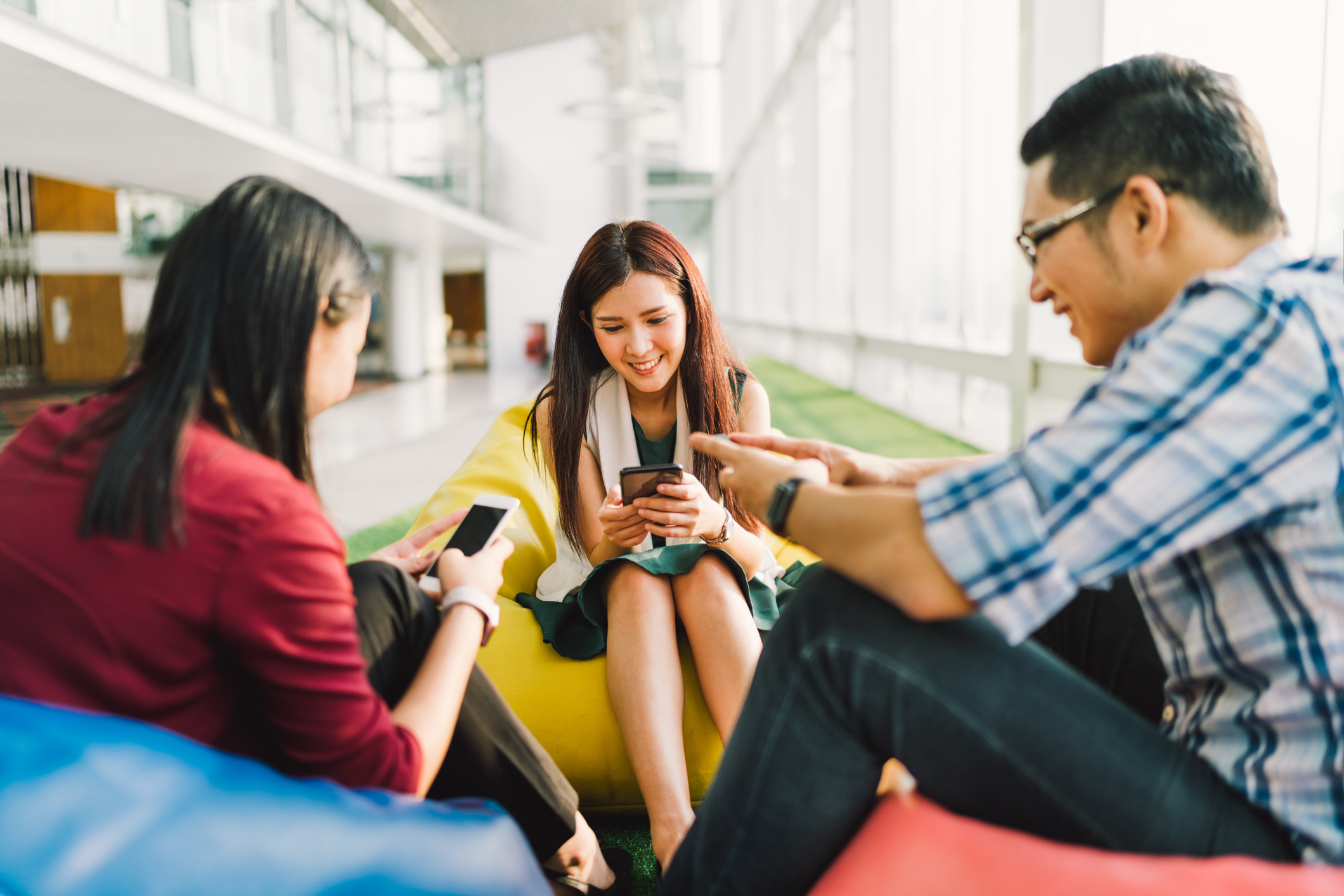 A group of Chinese youngsters sit on colorful beanbags, smiling at their smartphones.