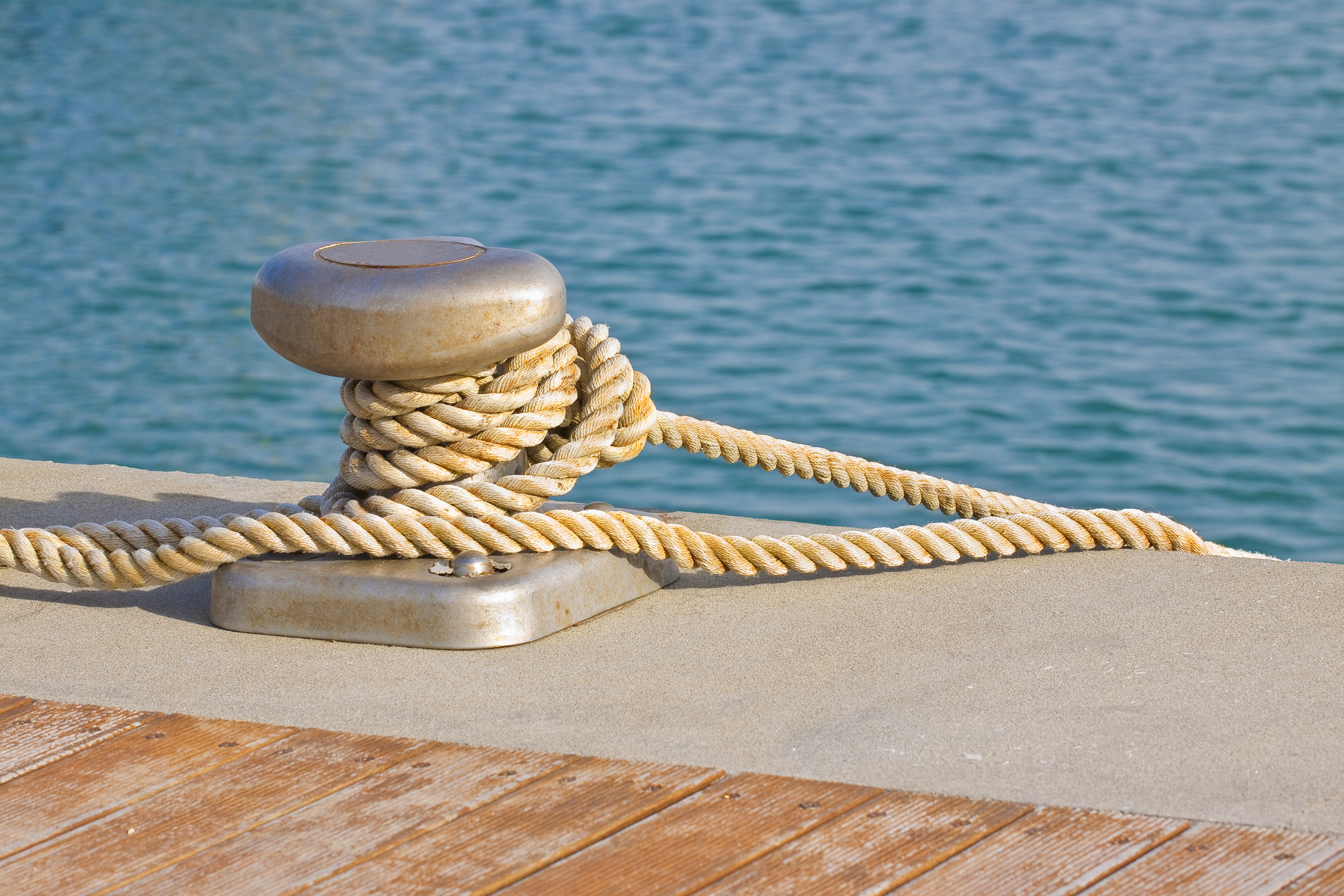 Close-up of a cleat for mooring boats with rope wrapped around it at waters' edge.