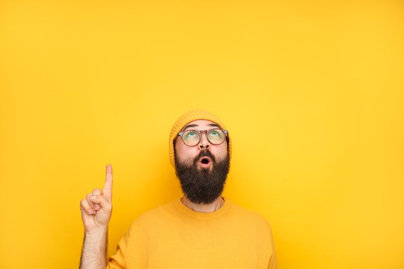 Man in bright yellow sweater and hat looking up and pointing with finger in excitement.