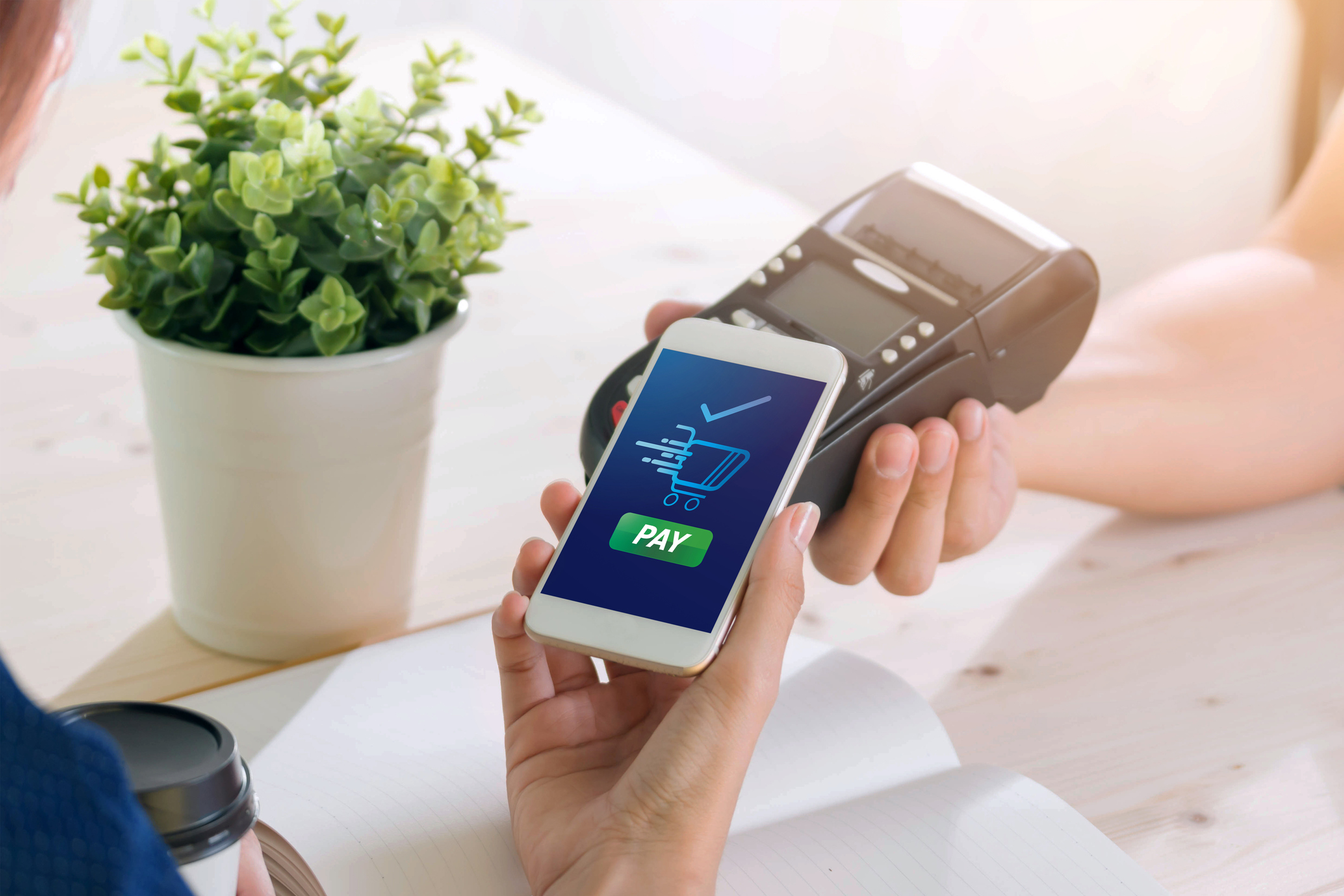 A hand holding a mobile phone up to a digital card reader at checkout.