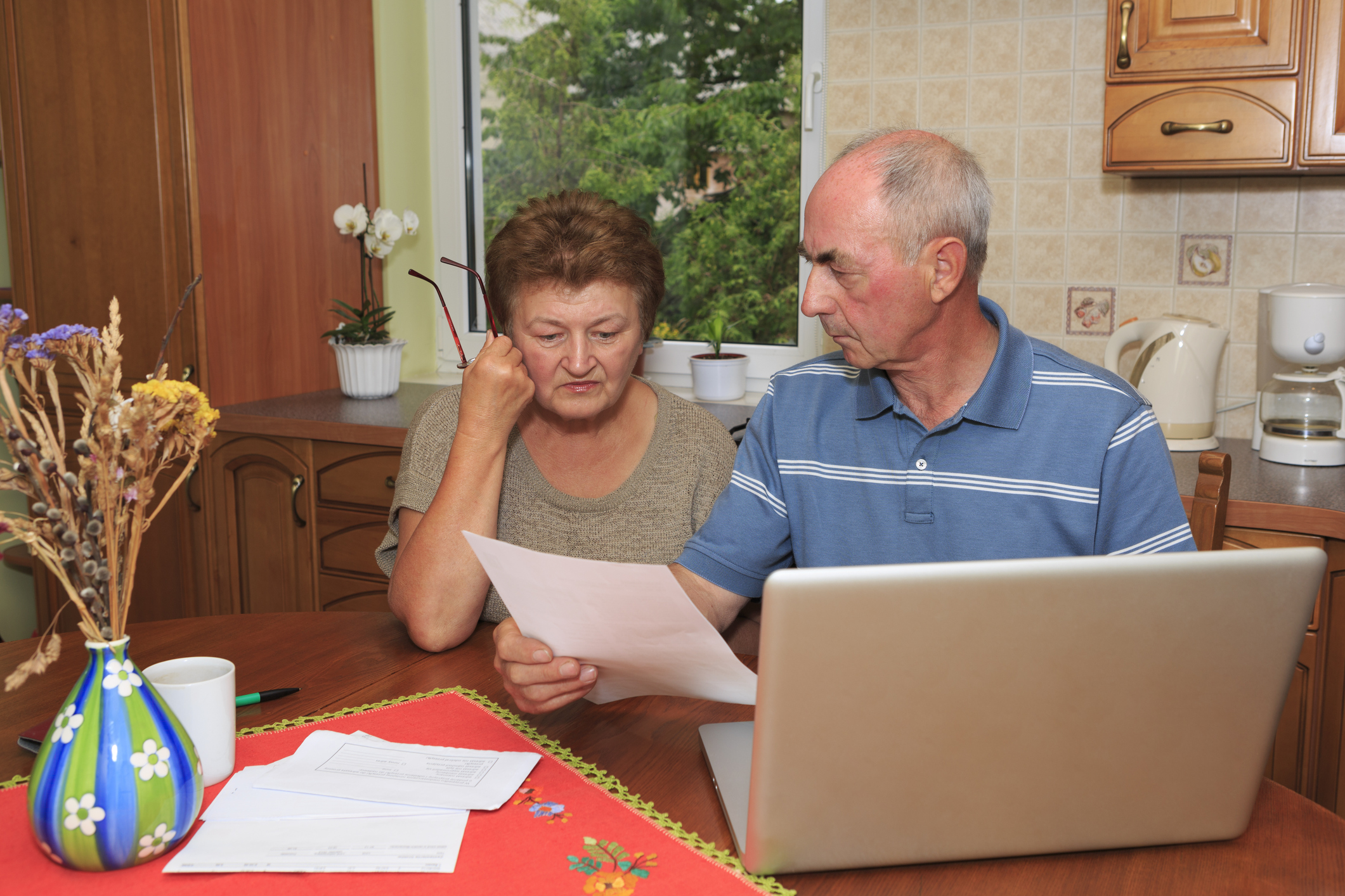 Older man and woman at a laptop looking at documents with serious expressions