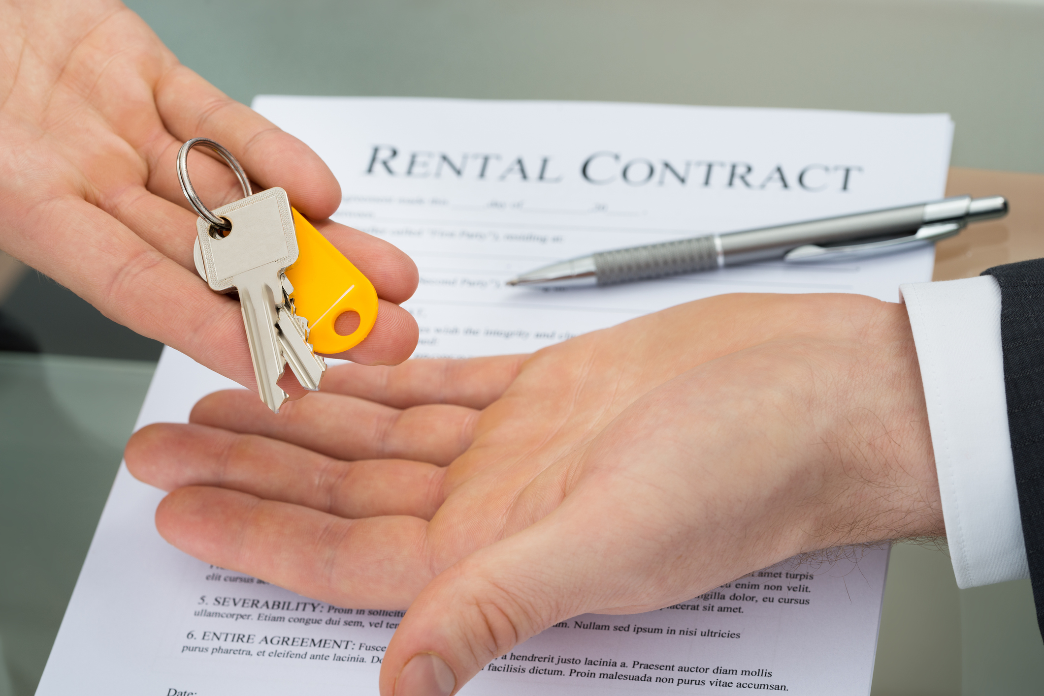 A person handing over keys, with a rental contract and pen on a table in the background.