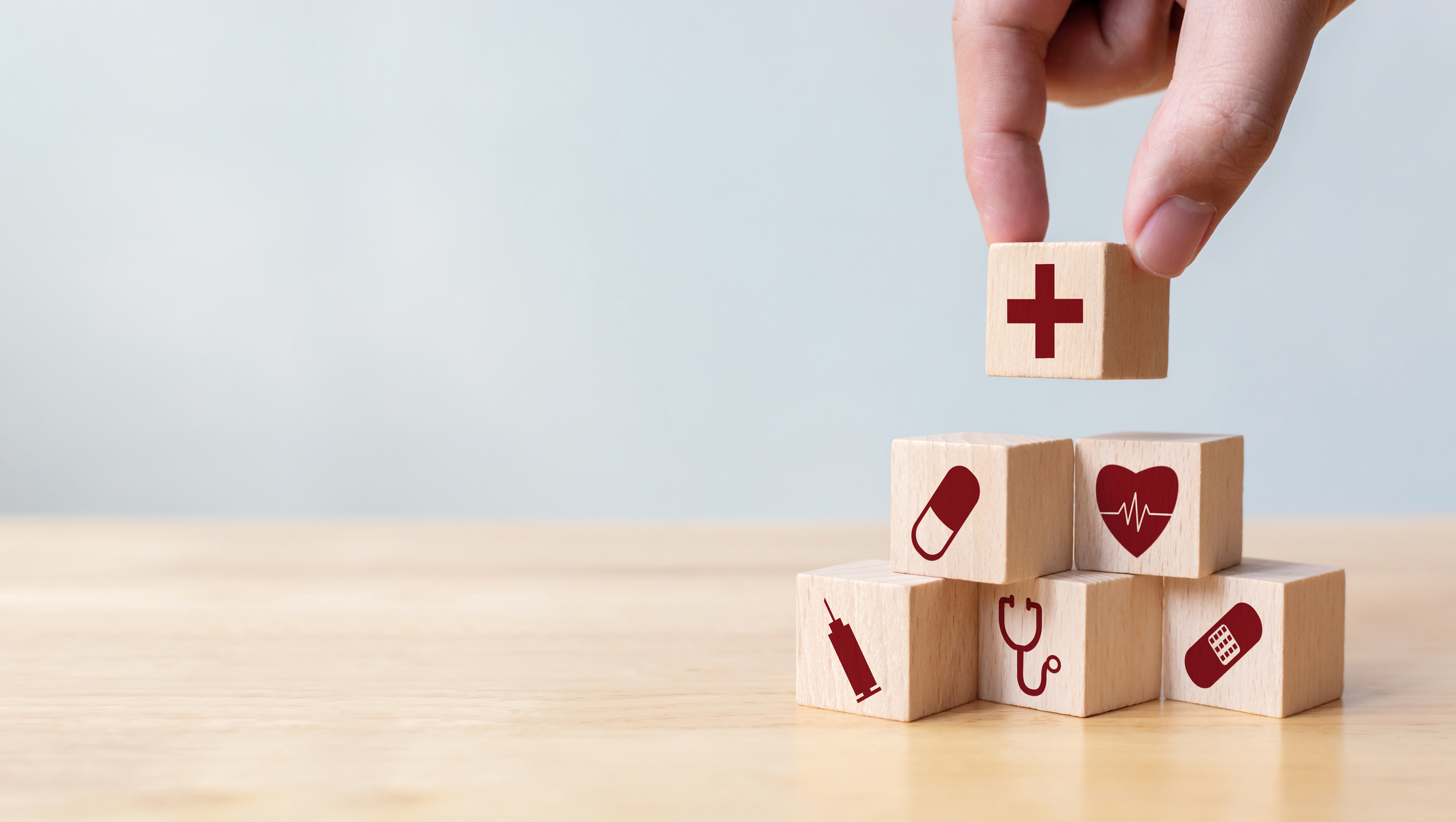 Wooden blocks with various healthcare symbols stacked into a pyramid on a wooden table top.